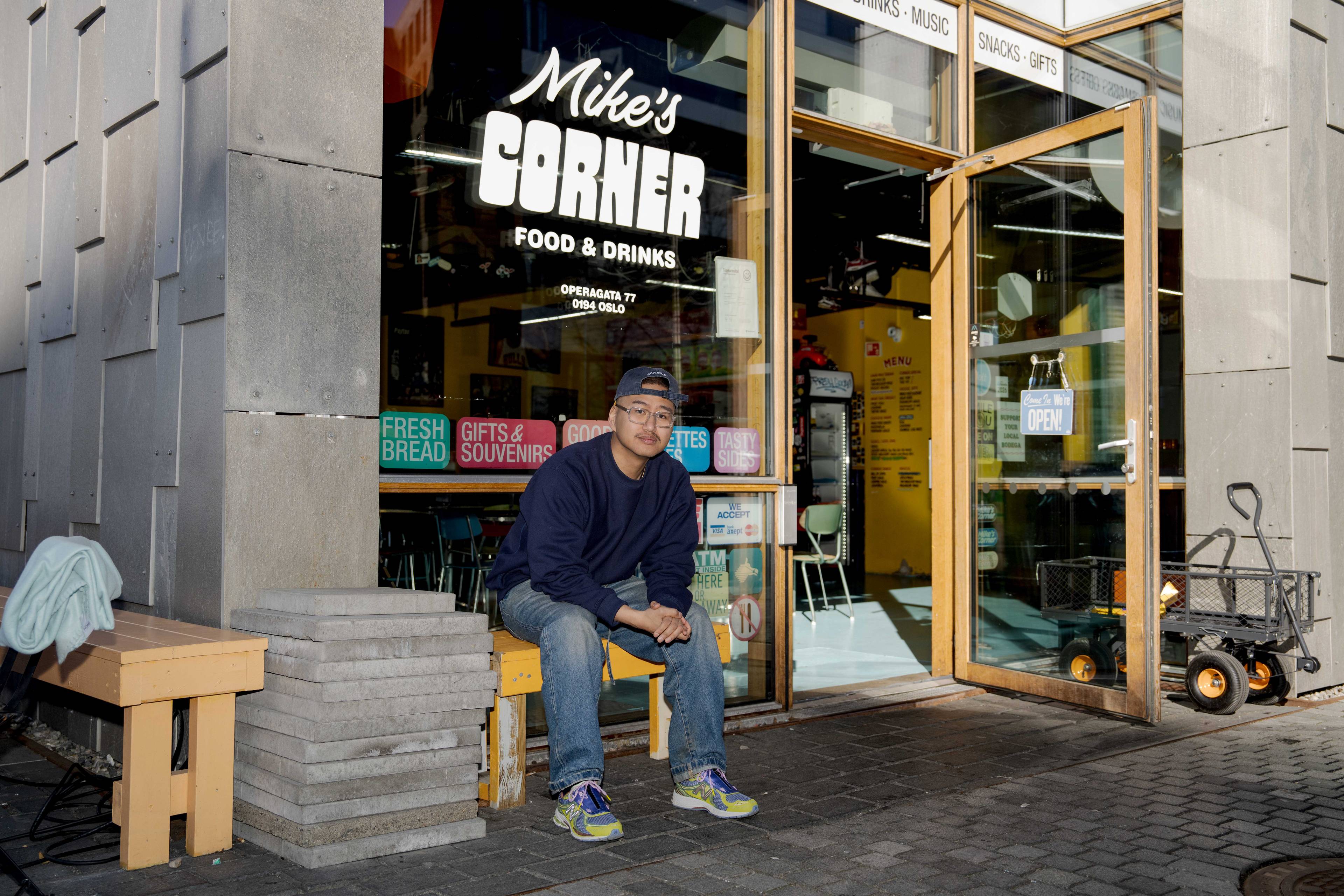 Mike sitter på en benk foran inngangen til sin restaurant Mike's Corner.
