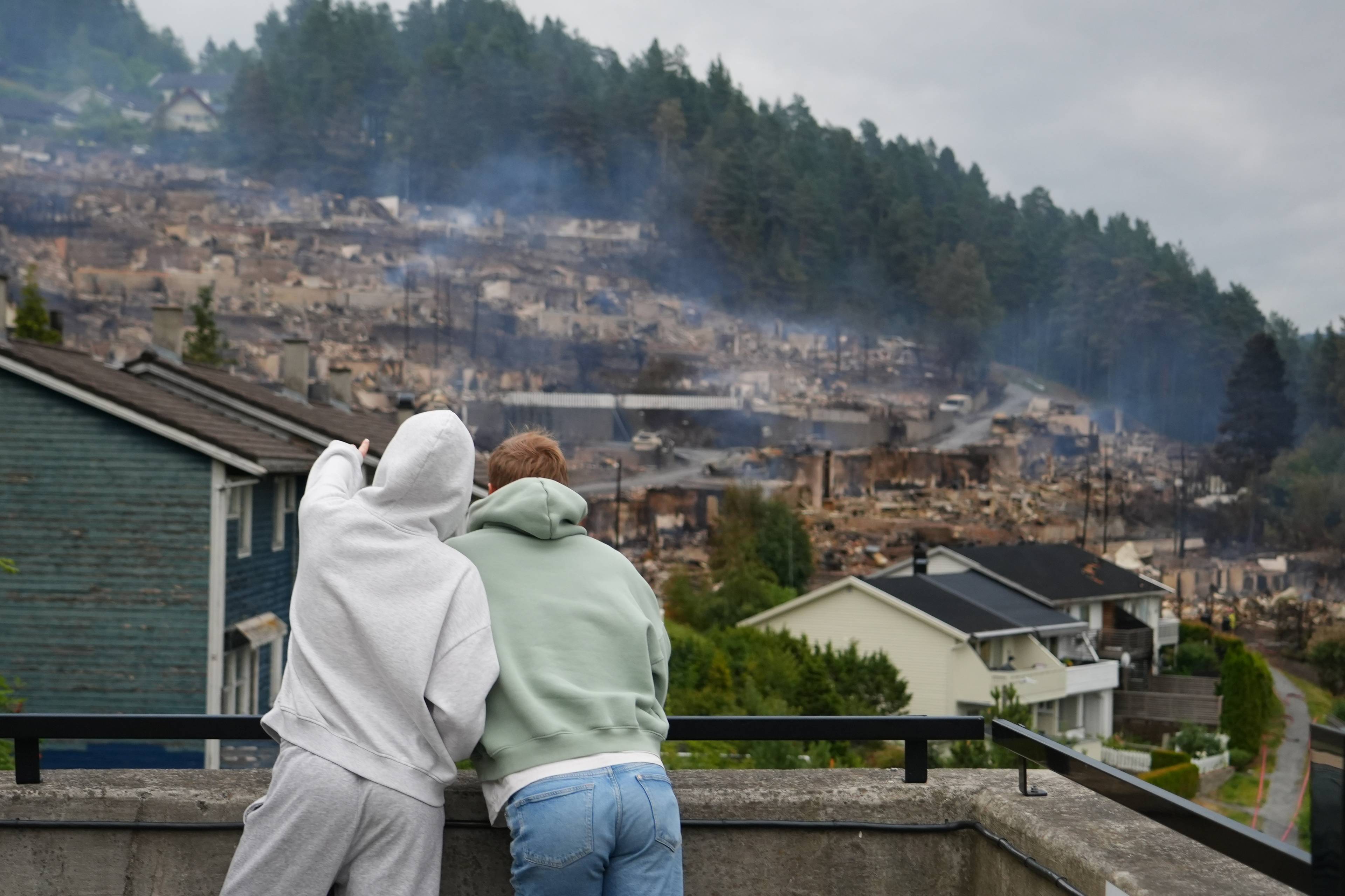 To personer ser utover et større område med nedbrente hus etter en brann. (Bildebeskrivelsen er laget av en KI-tjeneste)