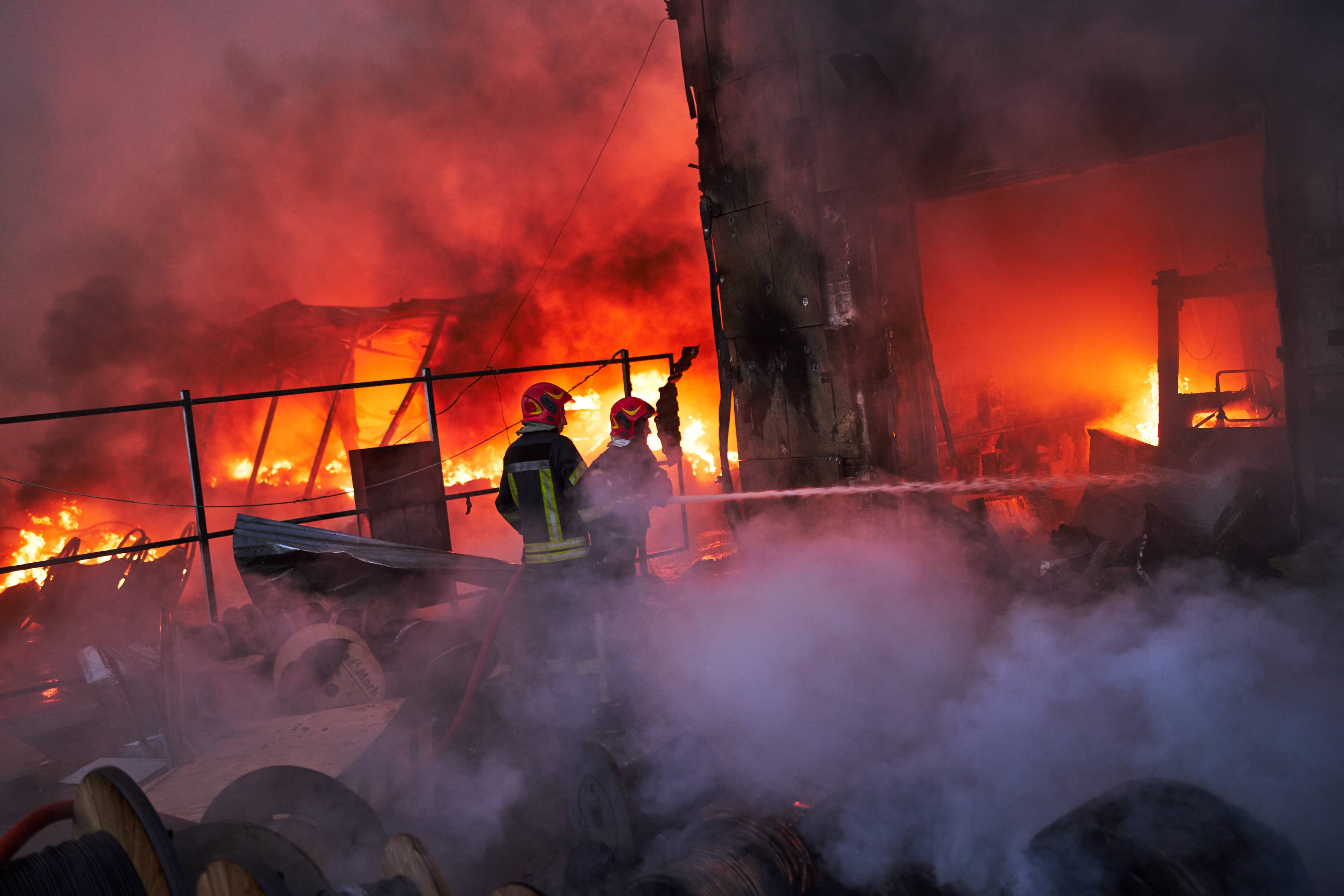Brannmannskaper slukker en kraftig brann i en industribygning. Store flammer og røyk preger området. (Bildebeskrivelsen er laget av en KI-tjeneste)
