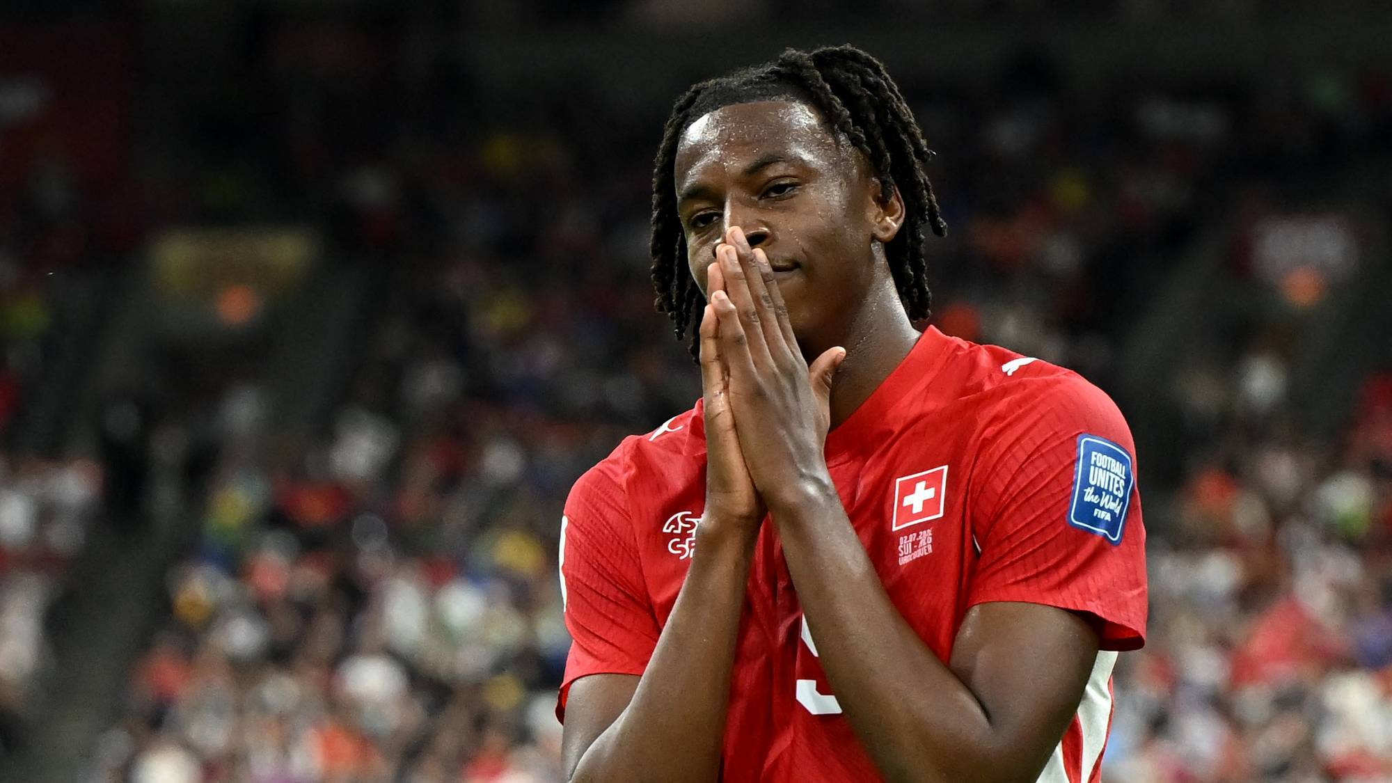 Sveitsisk fotballspiller i rød landslagsdrakt holder hendene samlet foran ansiktet på en bane. (Bildebeskrivelsen er laget av en KI-tjeneste)