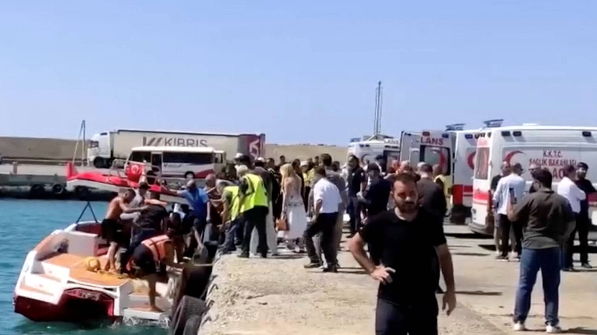 Folk går i land fra en båt ved en kai med ambulanser stående klare. (Bildebeskrivelsen er laget av en KI-tjeneste)