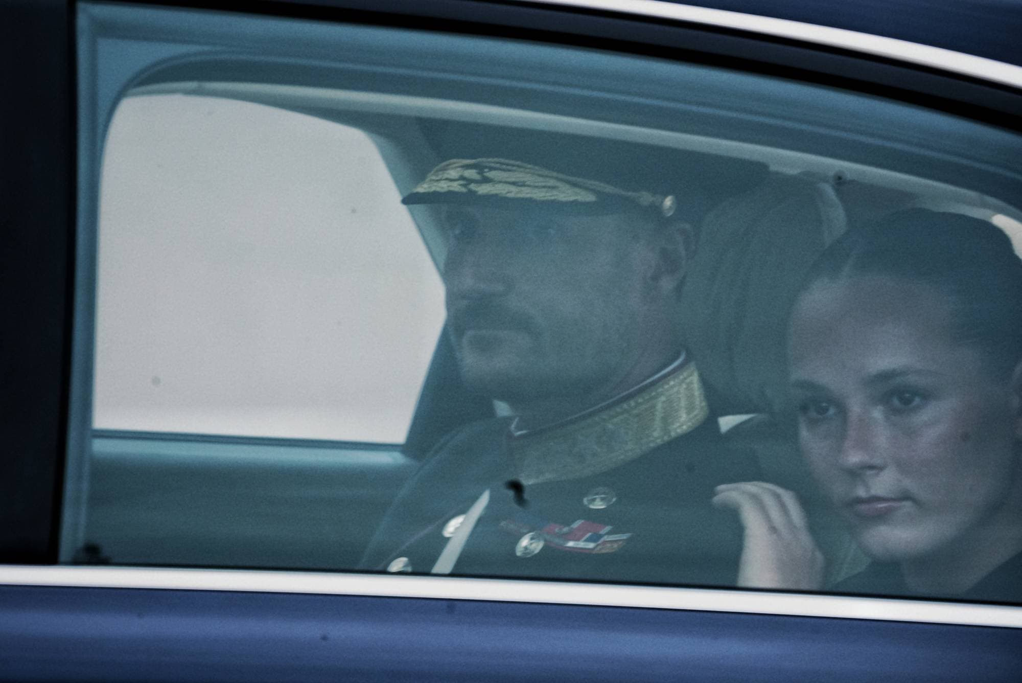 Den nye kongen i uniform sett gjennom et vindu i baksetet på en bil. Den nye kronprinsessen Ingrid Alexandra ved siden av ham.