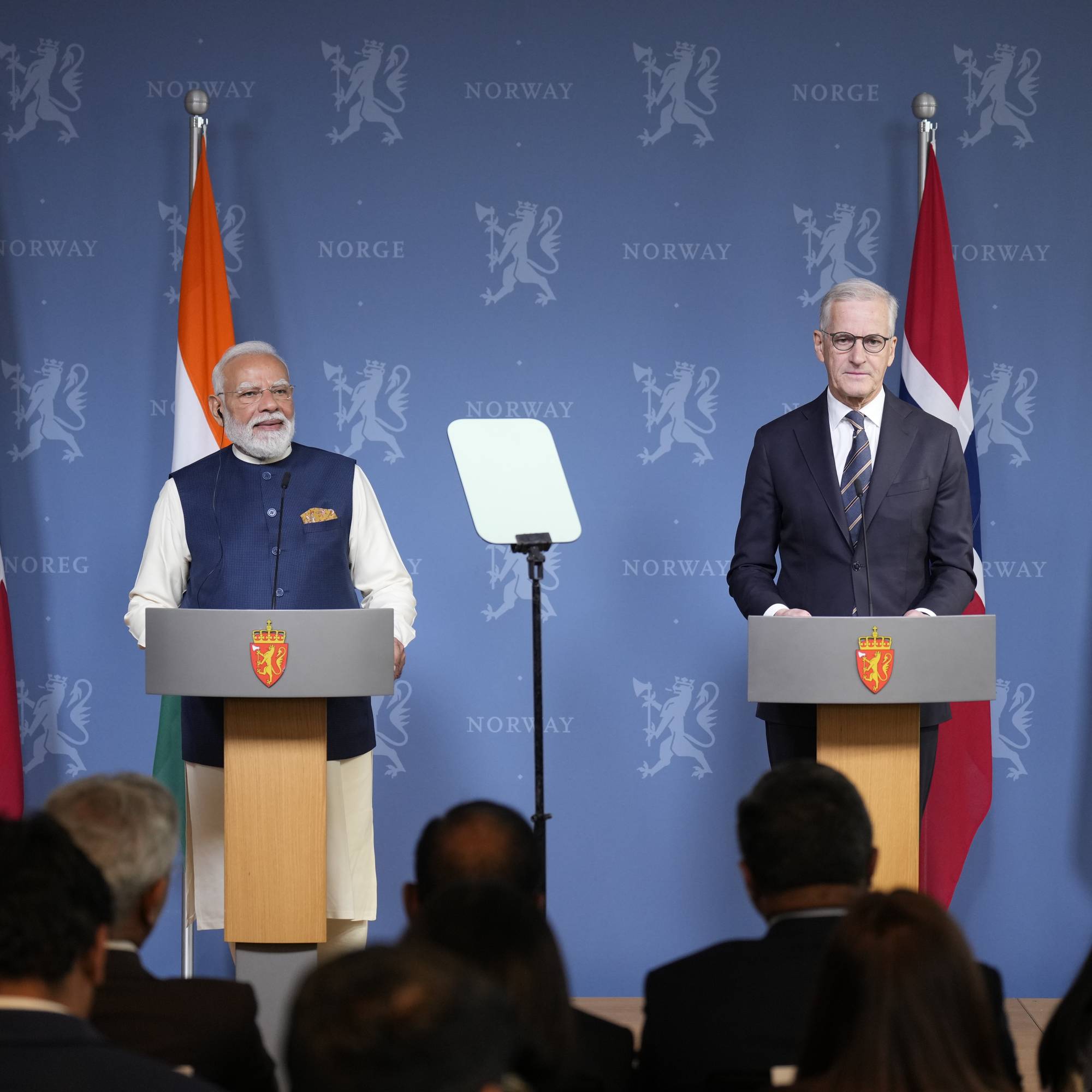 Norges statsminister Jonas Gahr Støre og Indias statsminister Narendra Modi holder pressekonferanse. De står bak podier foran norske og indiske flagg. Et publikum sitter foran dem. (Bildebeskrivelsen er laget av en KI-tjeneste)