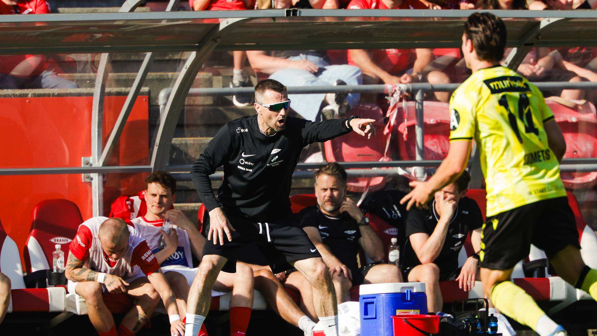 Fotballtrener gir instrukser til en spiller på sidelinjen under en kamp med Brann-spillere. 