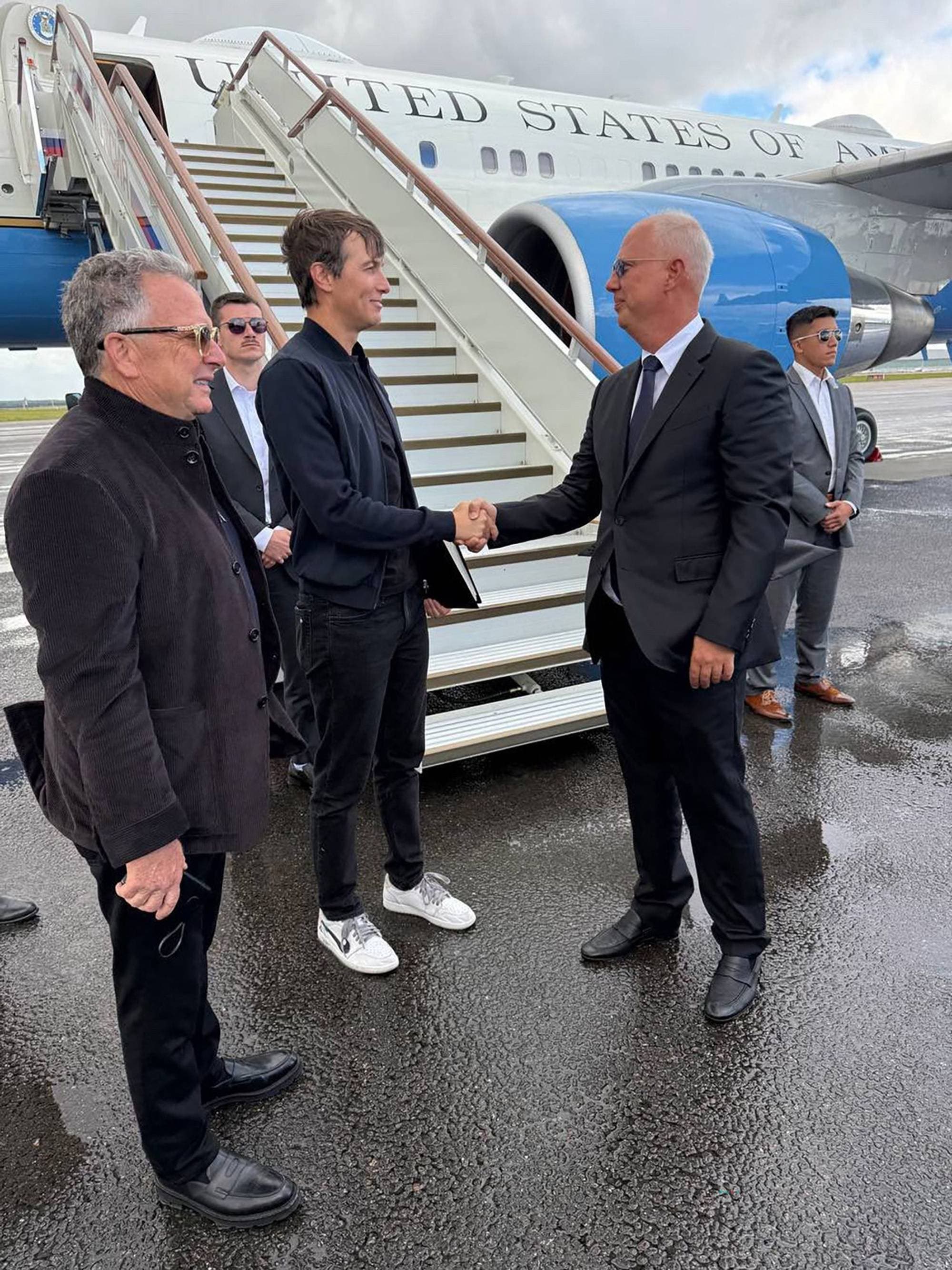 To menn håndhilser foran et fly fra United States of America. Andre menn står i bakgrunnen. (Bildebeskrivelsen er laget av en KI-tjeneste)