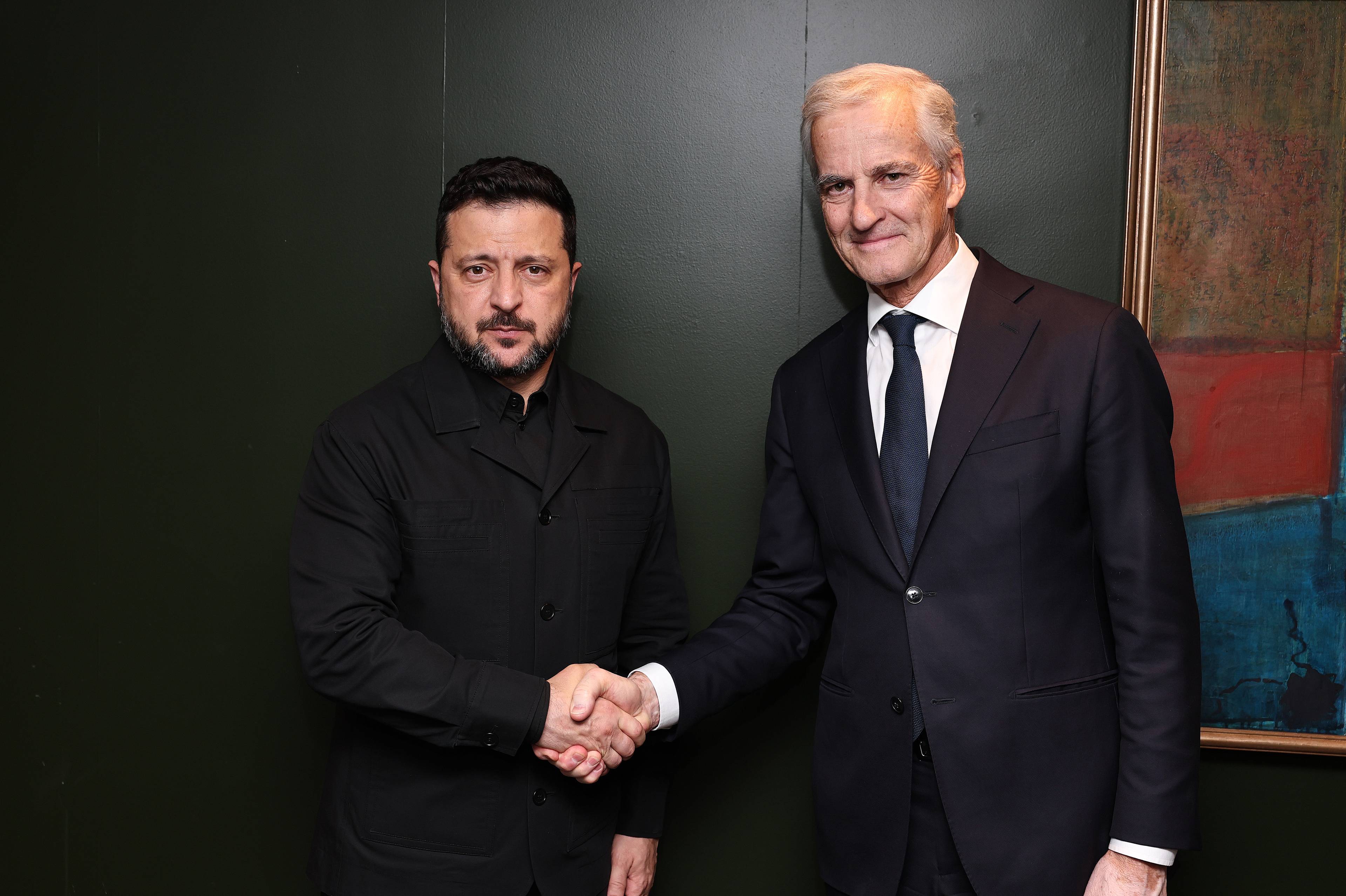 Volodymyr Zelenskyj og Jonas Gahr Støre håndhilser foran en mørk vegg. (Bildebeskrivelsen er laget av en KI-tjeneste)