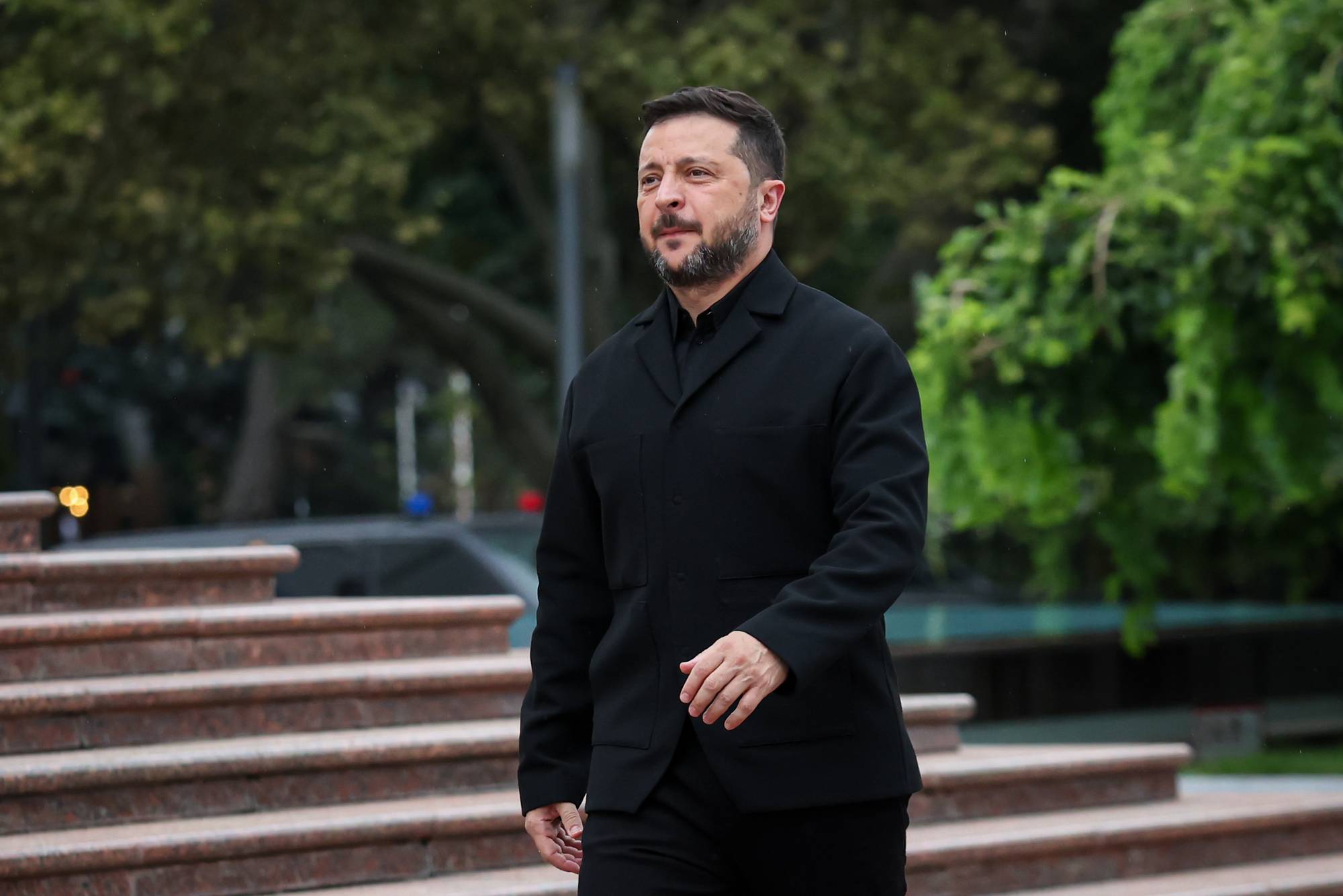 Ukrainas president Volodymyr Zelenskyj går ned en trapp utendørs, iført en svart jakke. (Bildebeskrivelsen er laget av en KI-tjeneste)