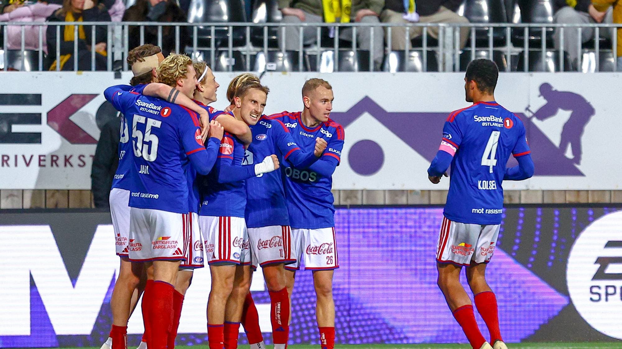 Fotballspillere i blå drakter jubler sammen etter en scoring på en fotballbane. (Bildebeskrivelsen er laget av en KI-tjeneste)