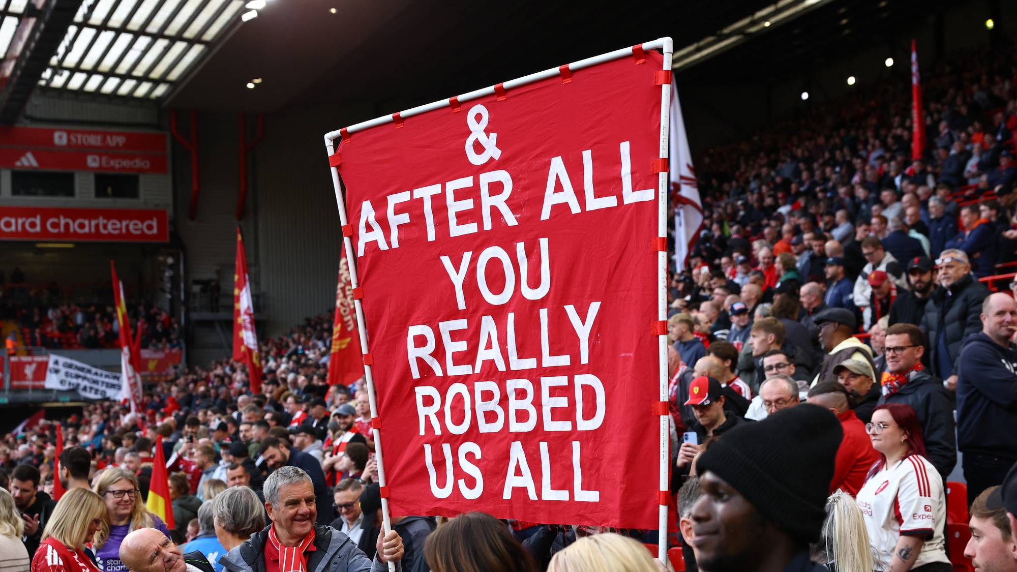 Supporter holder opp et rødt banner med teksten «& after all you really robbed us all» på tribune. (Bildebeskrivelsen er laget av en KI-tjeneste)