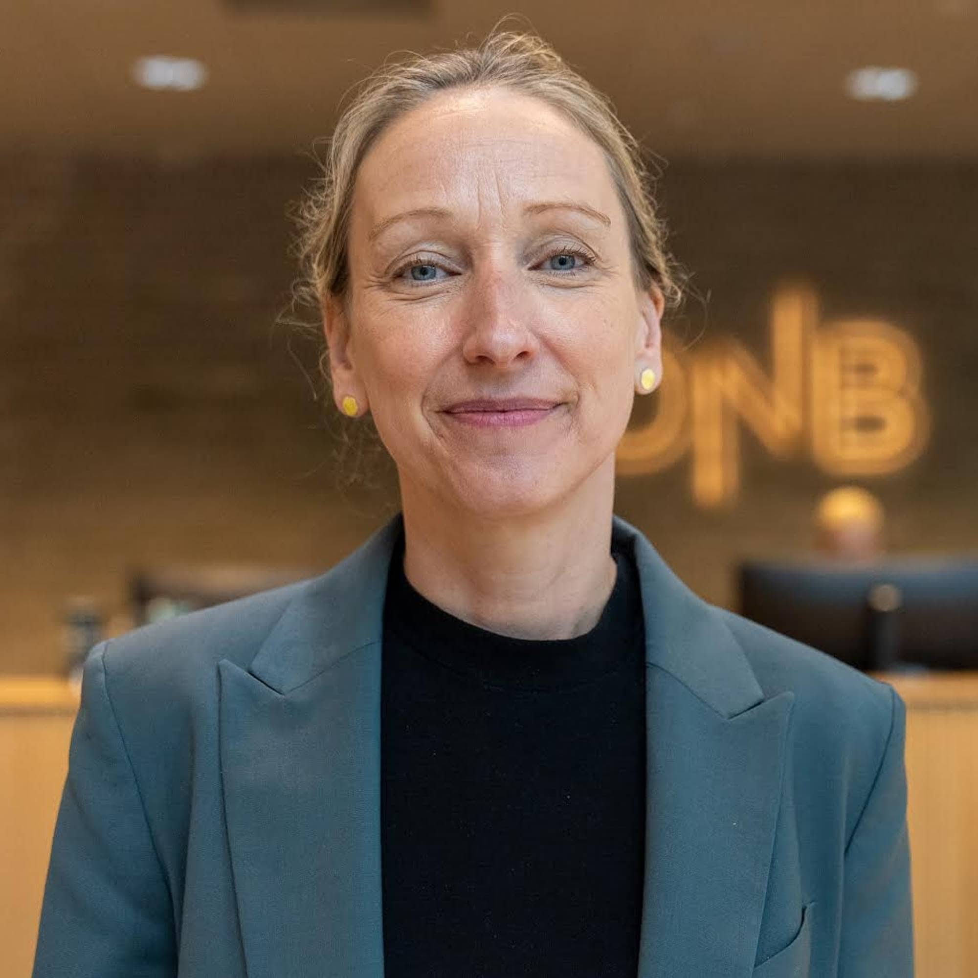Kvinne i grå blazer og svart overdel står føre DNB-resepsjonen. 