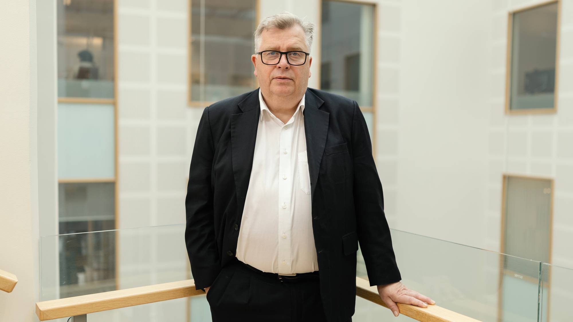 Mann i hvit skjorte, briller og dressjakke ser i kamera