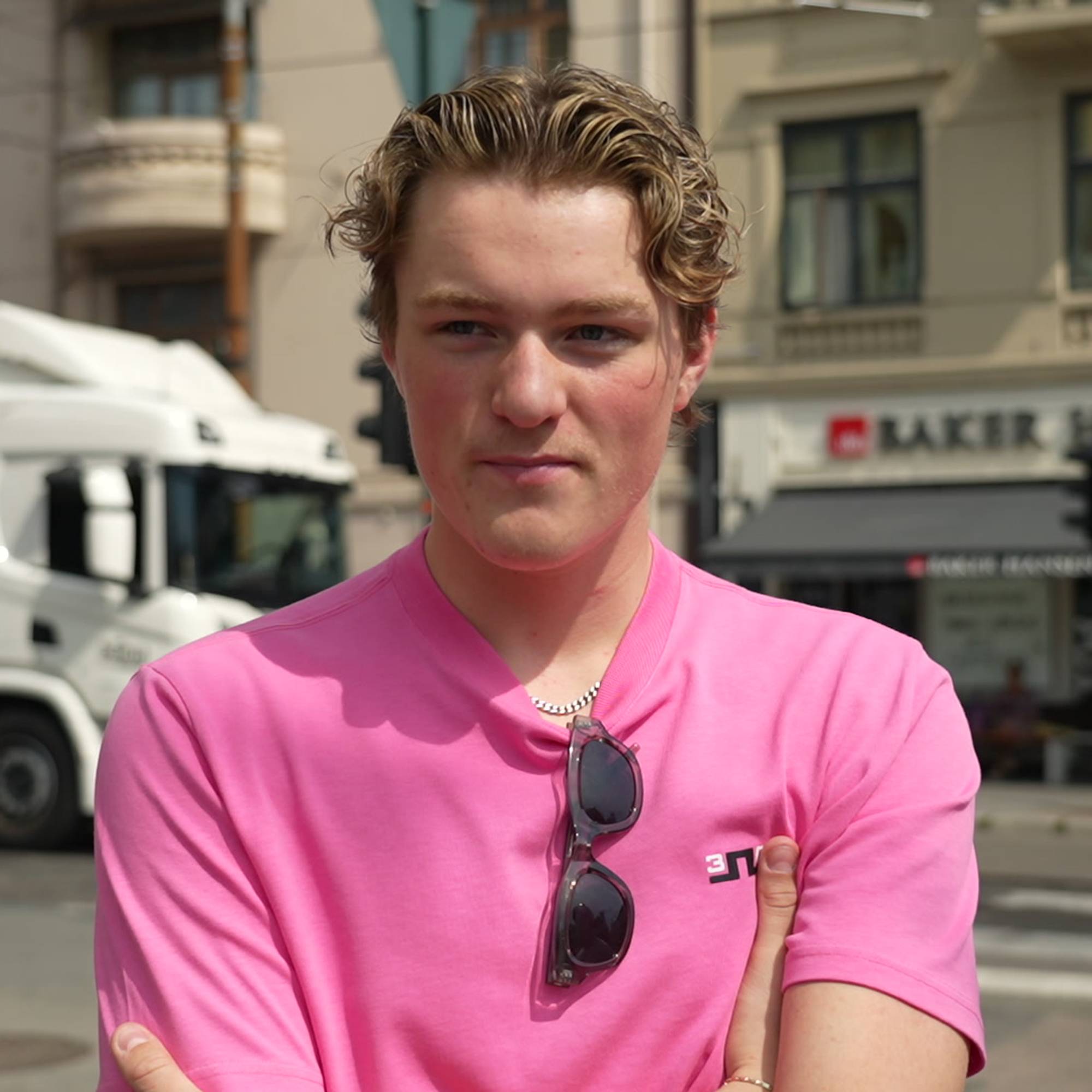 Ung mann i rosa t-skjorte står utendørs i en bygate. (Bildebeskrivelsen er laget av en KI-tjeneste)