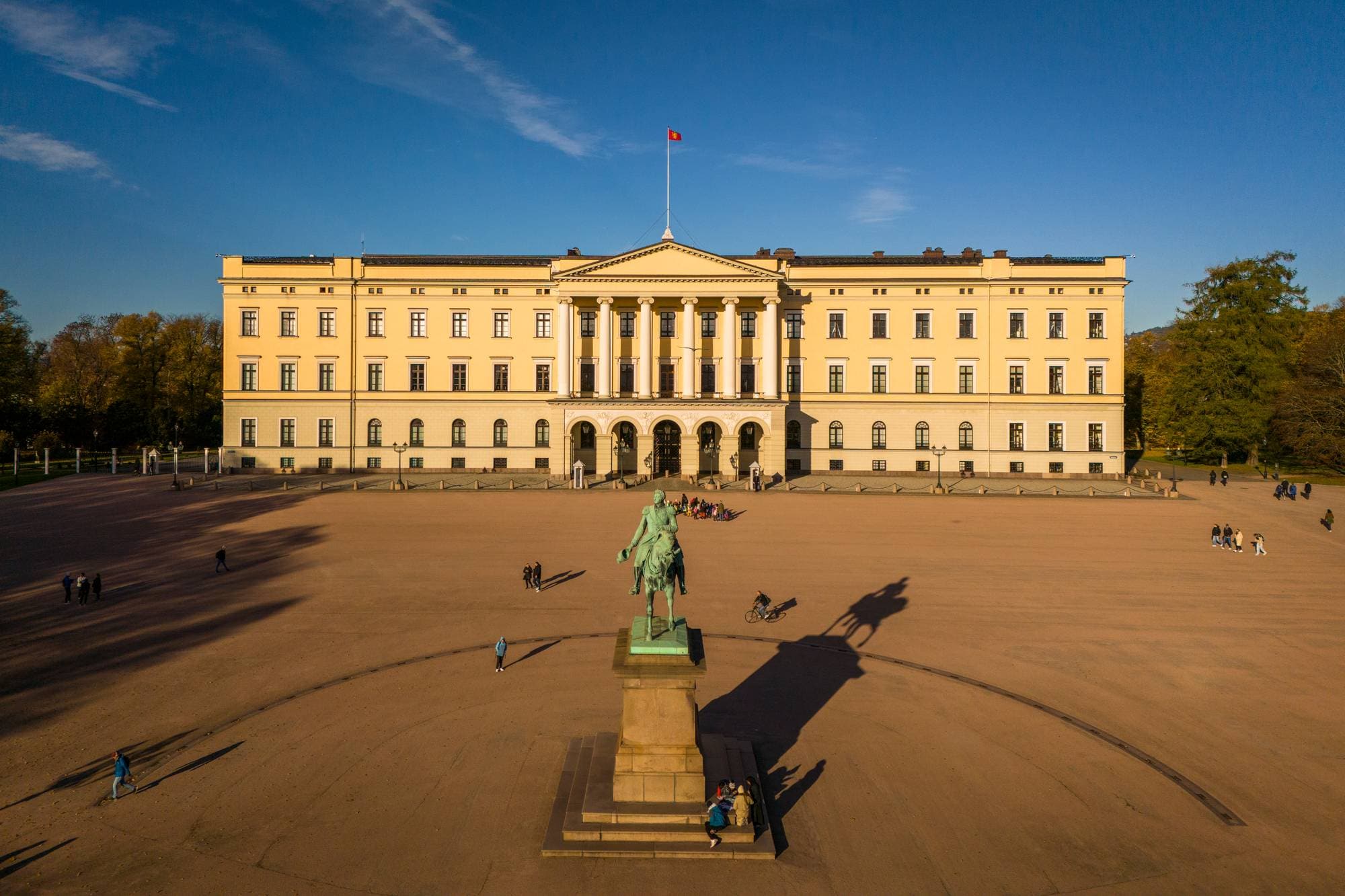Et dronebilde viser Slottet forfra, med rytterstatuen på Slottsplassen foran Slottet. På slottstaket er kongeflagget.