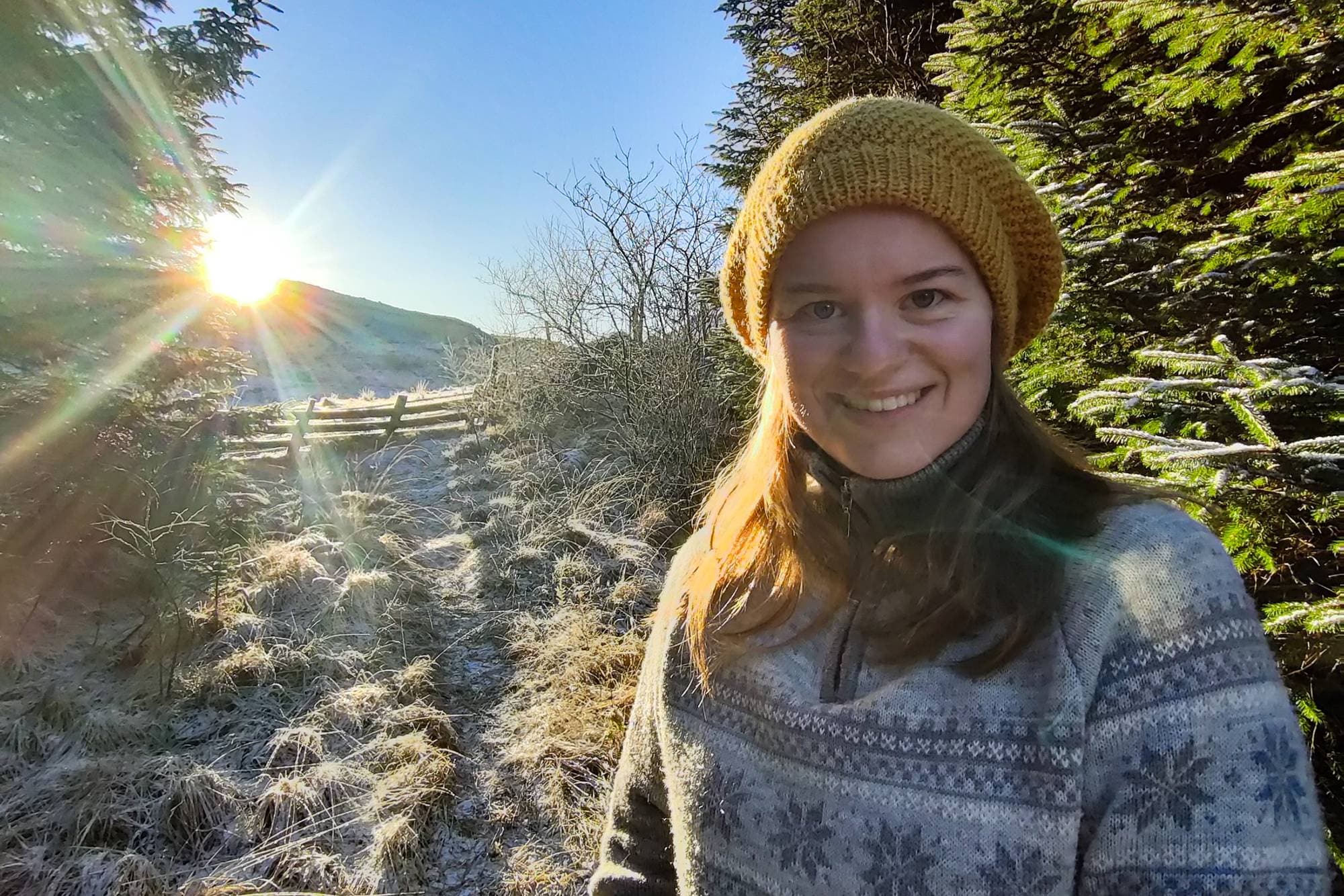Ida Terese (22) er i skogen med gul lue og ullgenser. Rundt henne ser man trer og bakke dekket av tynn snø.