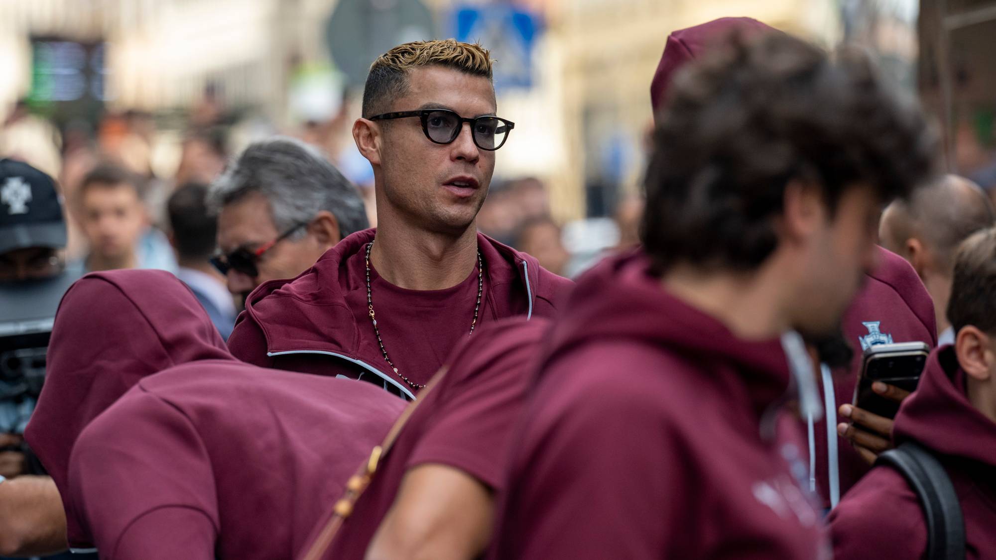 Cristiano Ronaldo i briller sammen med andre i røde hettejakker i en folkemengde. (Bildebeskrivelsen er laget av en KI-tjeneste)