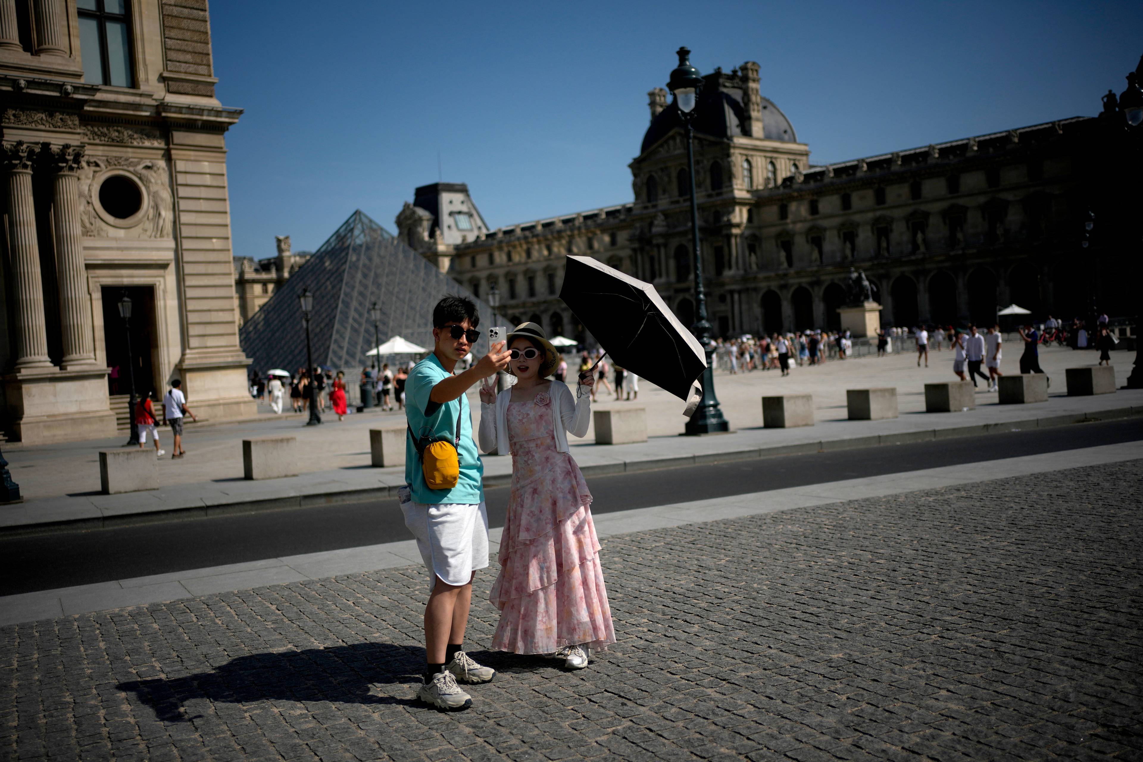 Turister tar bilde med en paraply utenfor Louvre