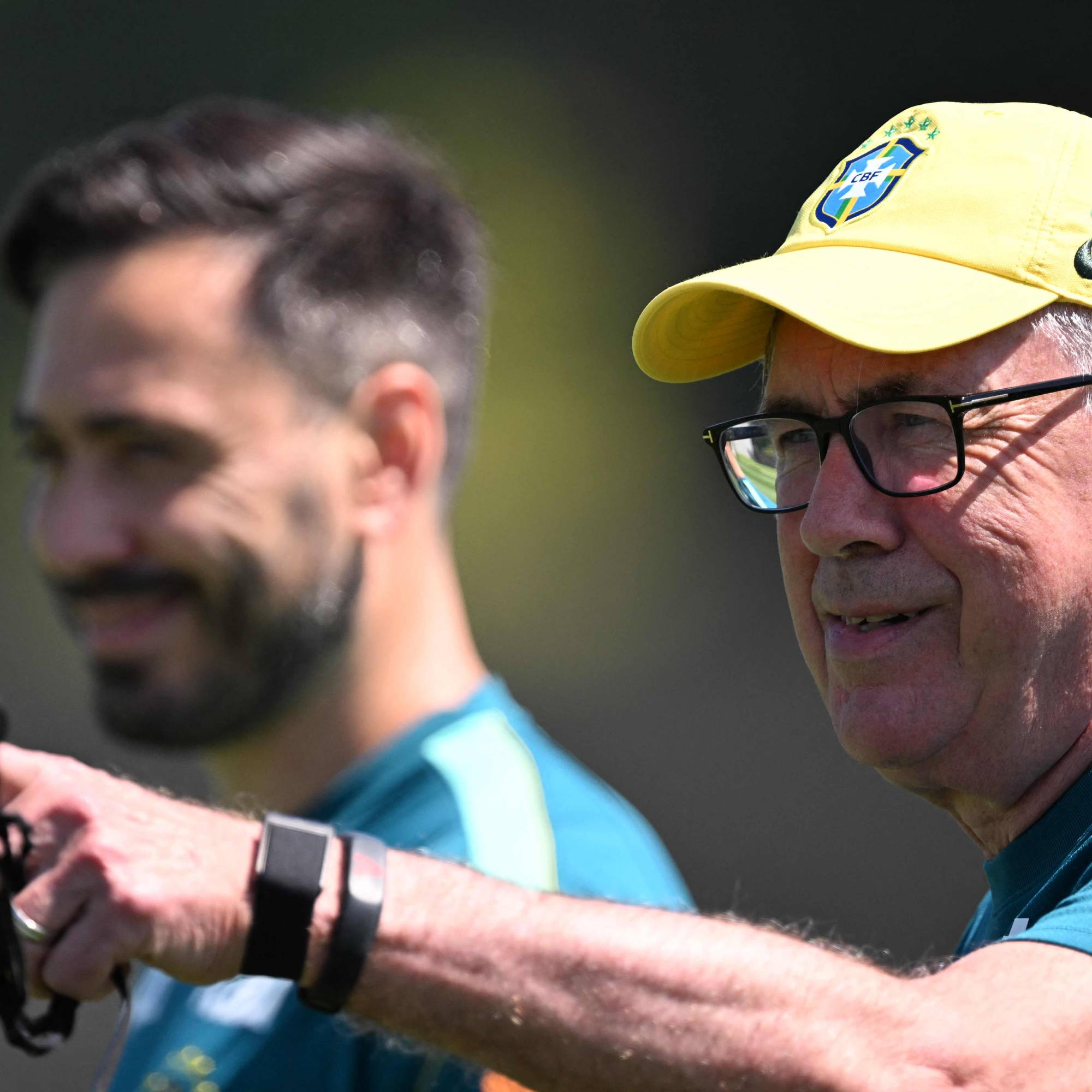 Carlo Ancelotti i gul landslagscaps peker utover under en treningsøkt. En annen person er i bakgrunnen. (Bildebeskrivelsen er laget av en KI-tjeneste)
