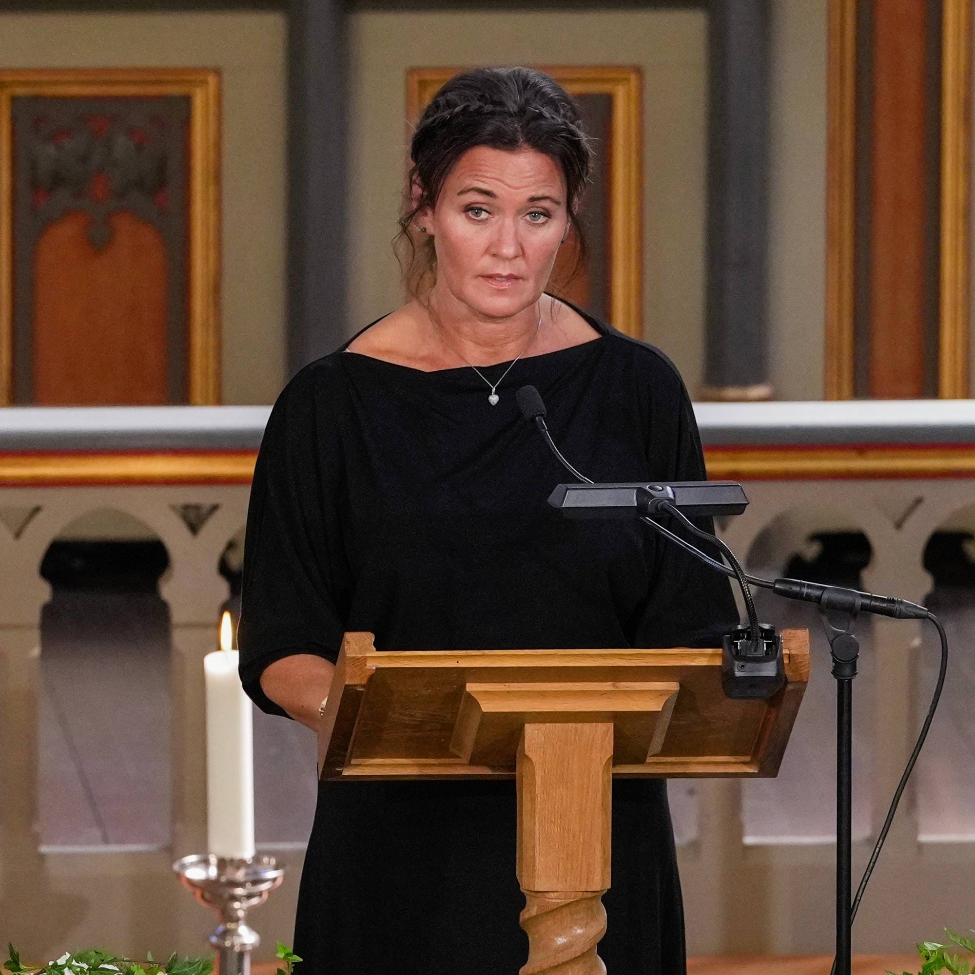 En kvinne i svart holder tale fra en talerstol i en kirke med en prest ved siden av seg.