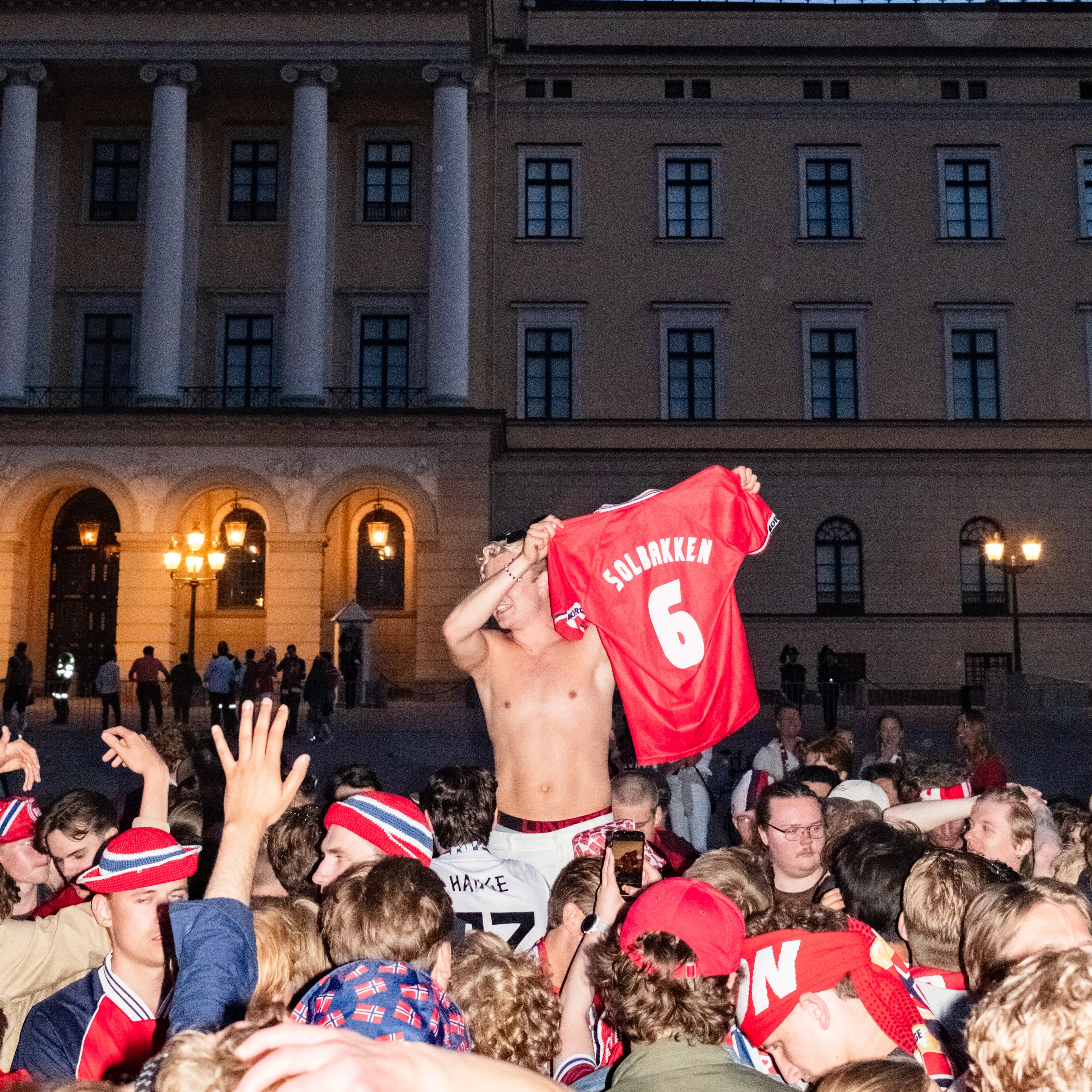 Person holder opp en rød fotballdrakt med navnet Solbakken foran Slottet med en folkemengde.