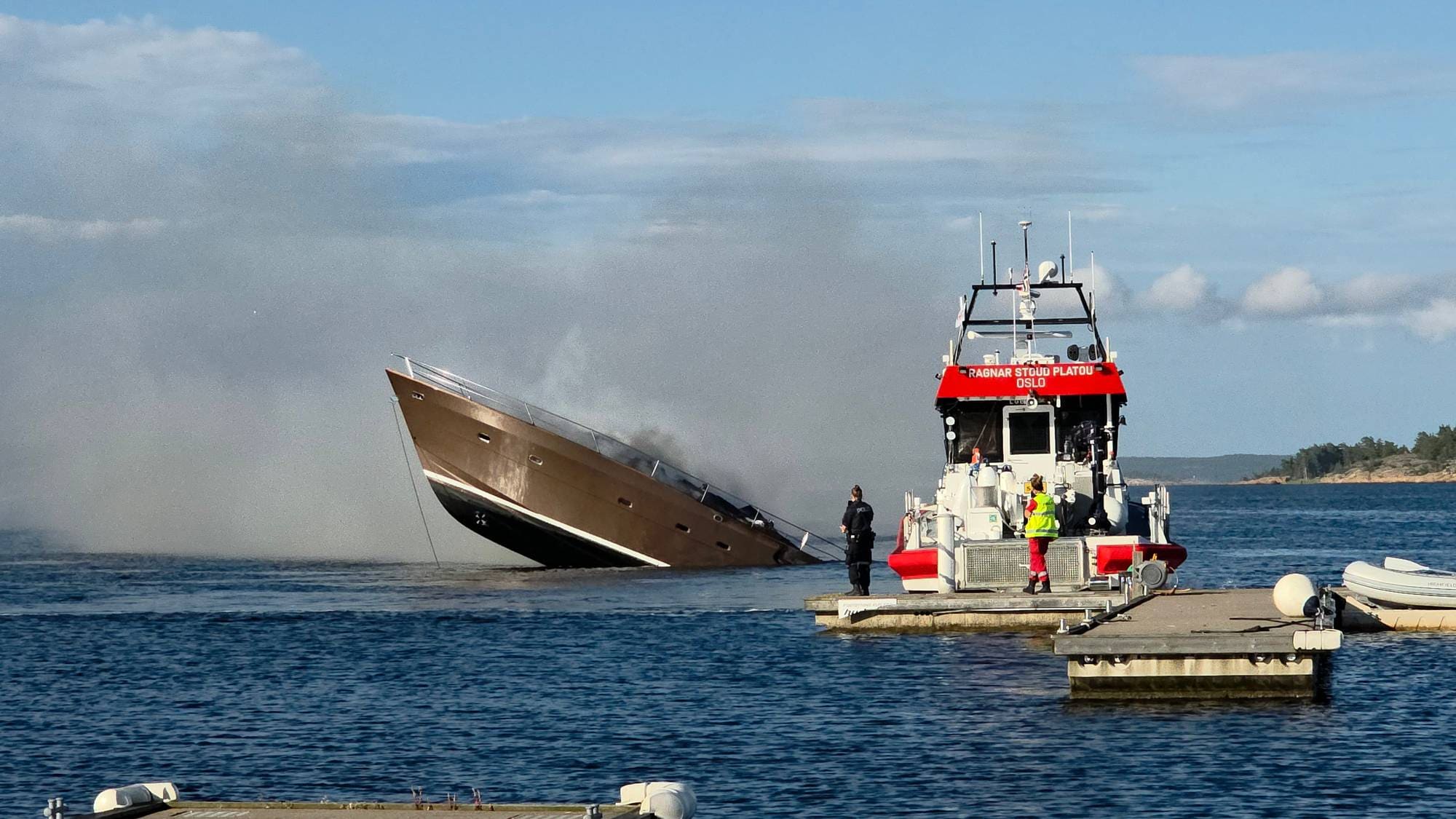 En brennende luksusyacht synker ved en brygge der redningsskøyta Ragnar Stoud Platou ligger til. (Bildebeskrivelsen er laget av en KI-tjeneste)