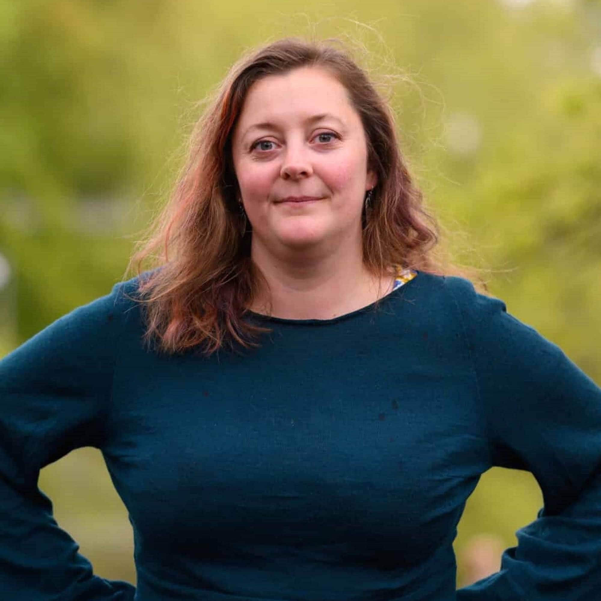 Kvinne med halvlangt, brunt hår står foran en uklar, grønn bakgrunn. Hun bærer en mørkegrønn genser. (Bildebeskrivelsen er laget av en KI-tjeneste)