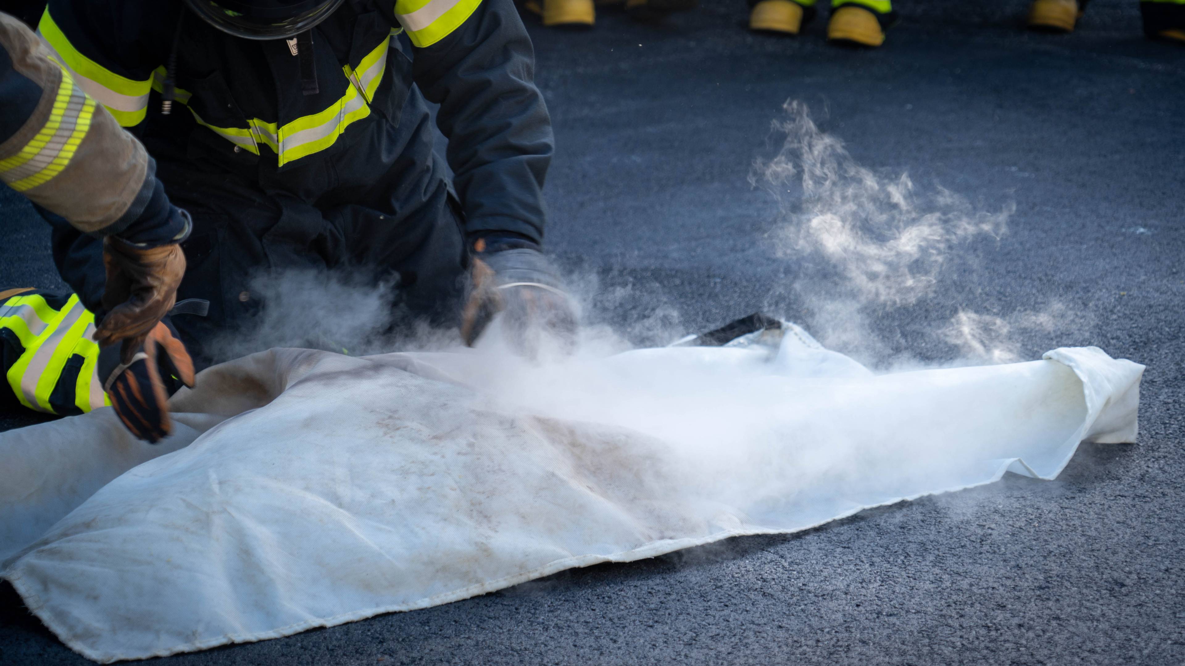 Brannkonstabel som slukker flammer med brannteppe.