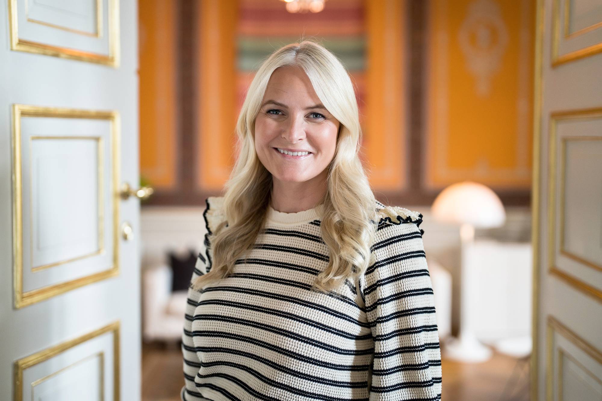 Kronprinsesse Mette-Marit står i døren inn til kontoret sitt på Slottet, hun ser rett i kamera og smiler