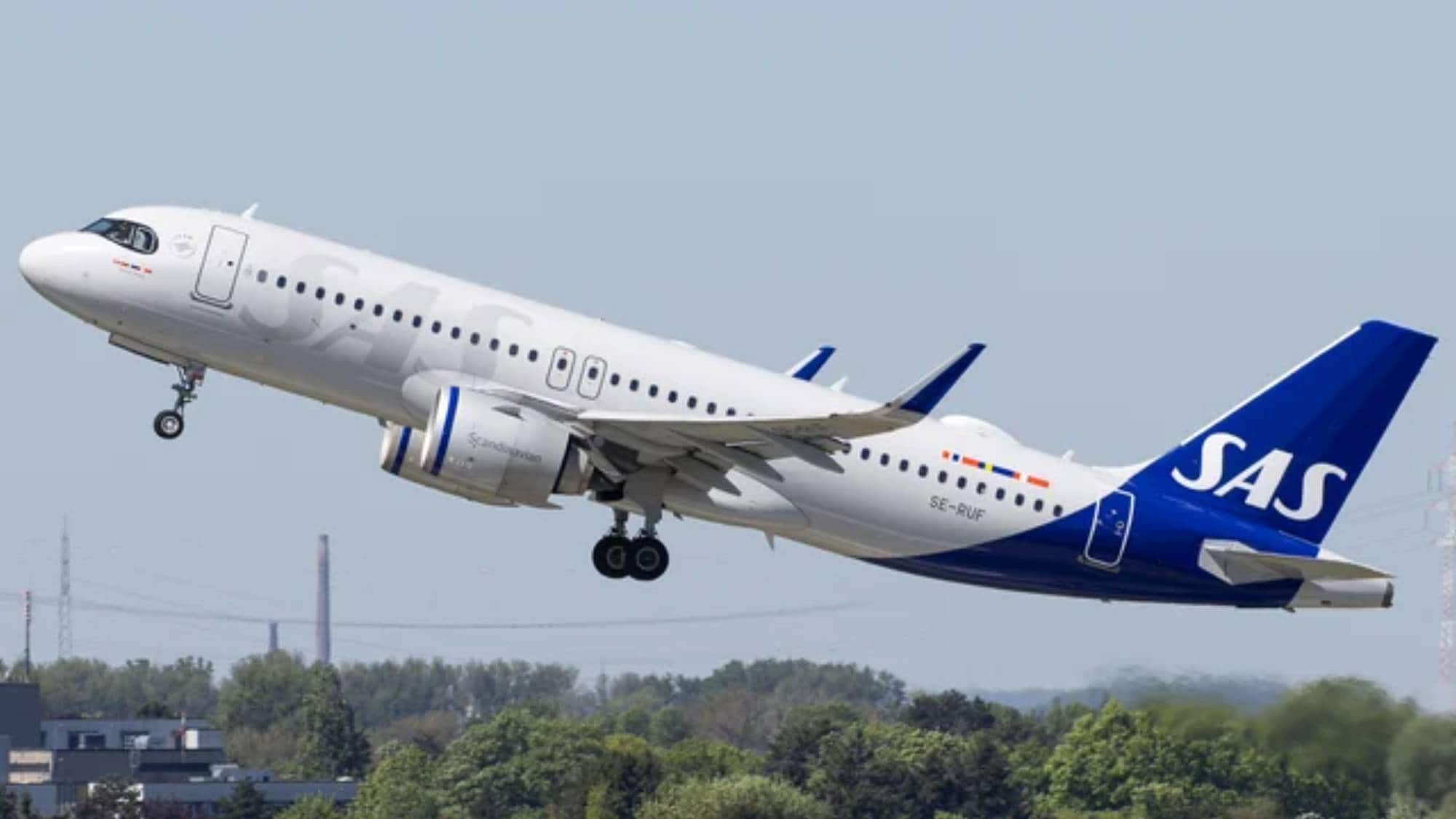 SAS-fly - Hvitt fly med blå hale og SAS skrevet i hvitt på halen letter fra en flyplass
