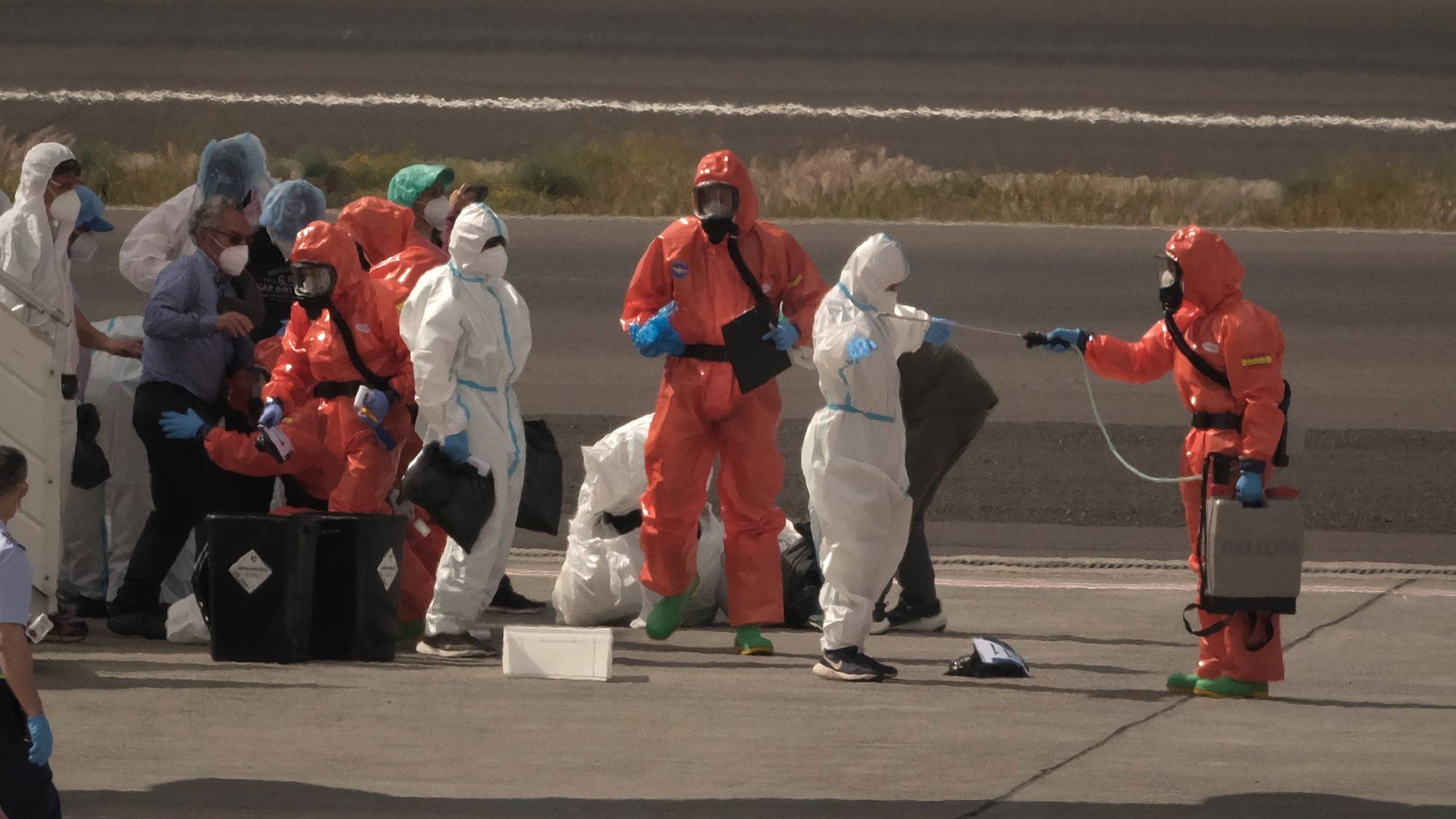 Personer i oransje og hvite verneutstyr utfører dekontaminering utendørs. En person i oransje drakt holder en sprøyte med en slange. Andre personer står ved siden av og ser på. 