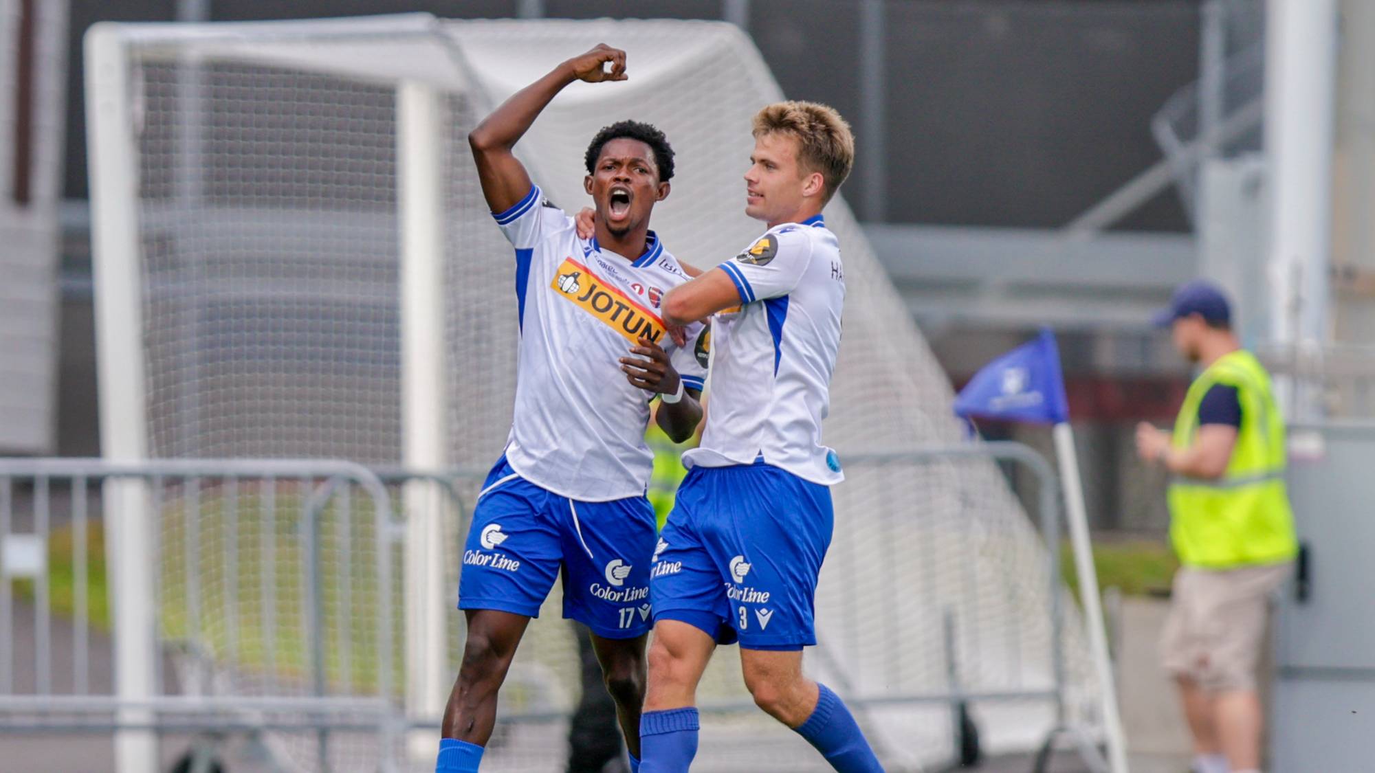 To fotballspillere i hvite og blå drakter jubler for mål på en fotballbane. (Bildebeskrivelsen er laget av en KI-tjeneste)