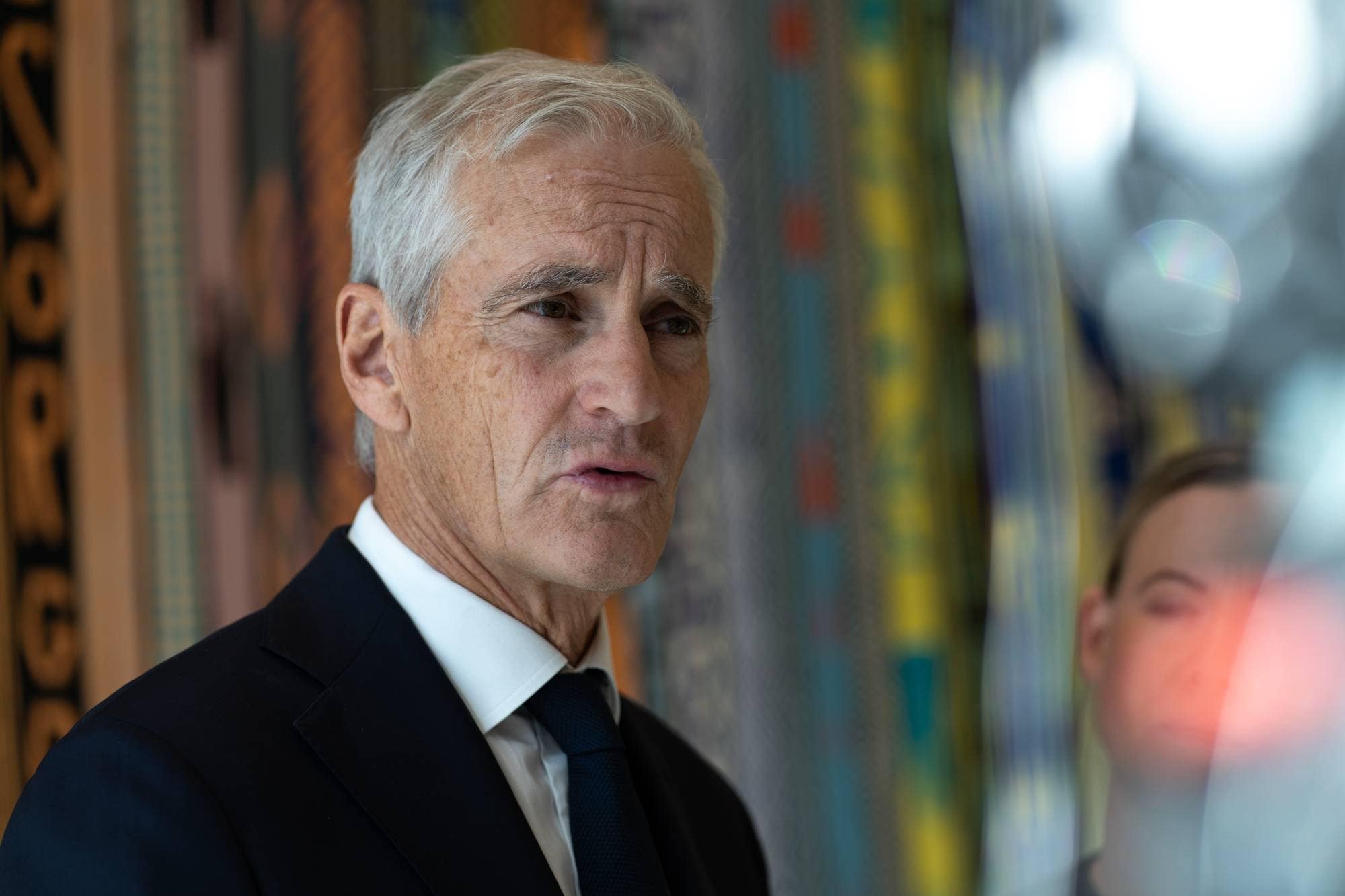 Jonas Gahr Støre snakker til NRK med en fargerik vegg i bakgrunn
