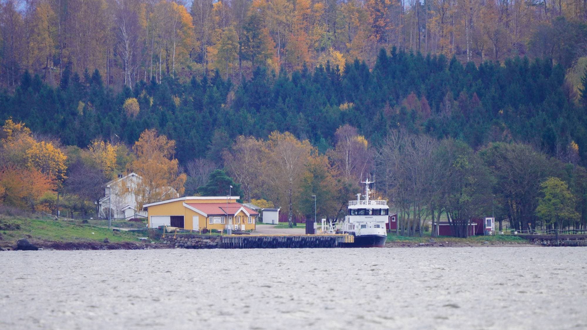 Båt, hus, brygge og trær ved vannet. 