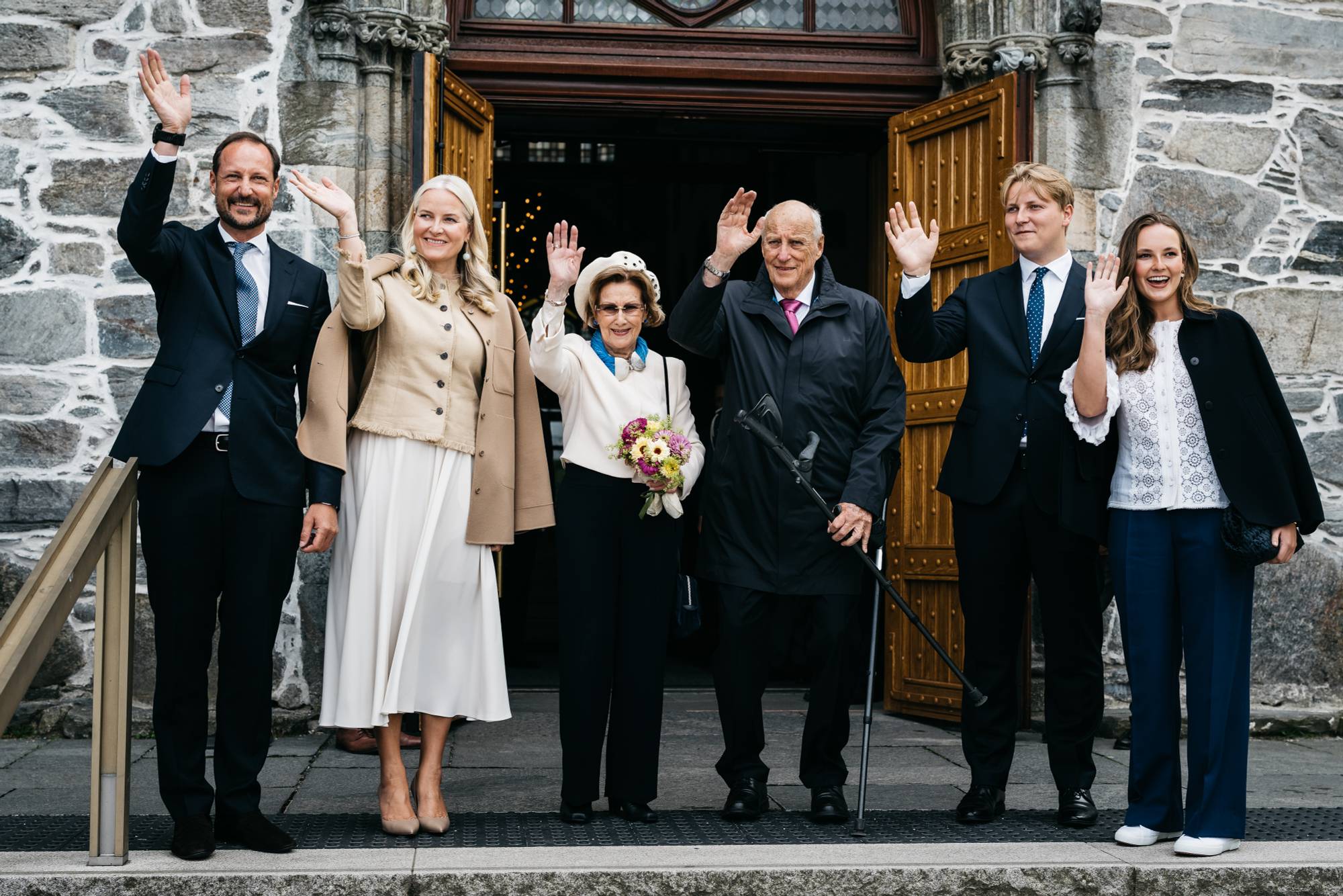Kongefamilien står ved siden av hverandre og vinker når de står utenfor domkirken i Stavanger i juli 2025.