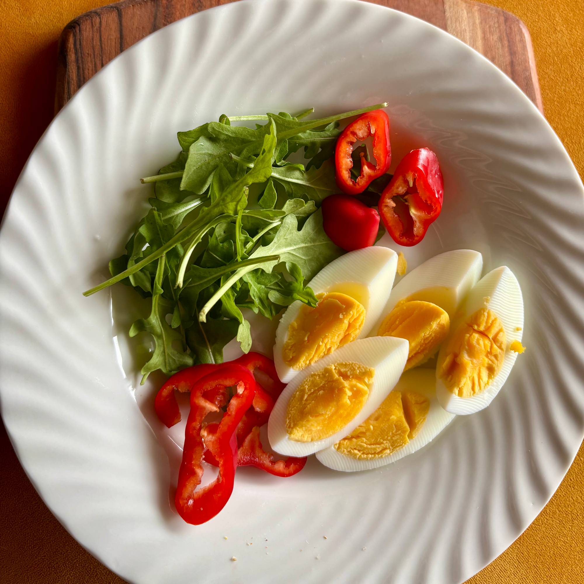 Et hvitt fat med egg, ruccolasalat og paprika på.