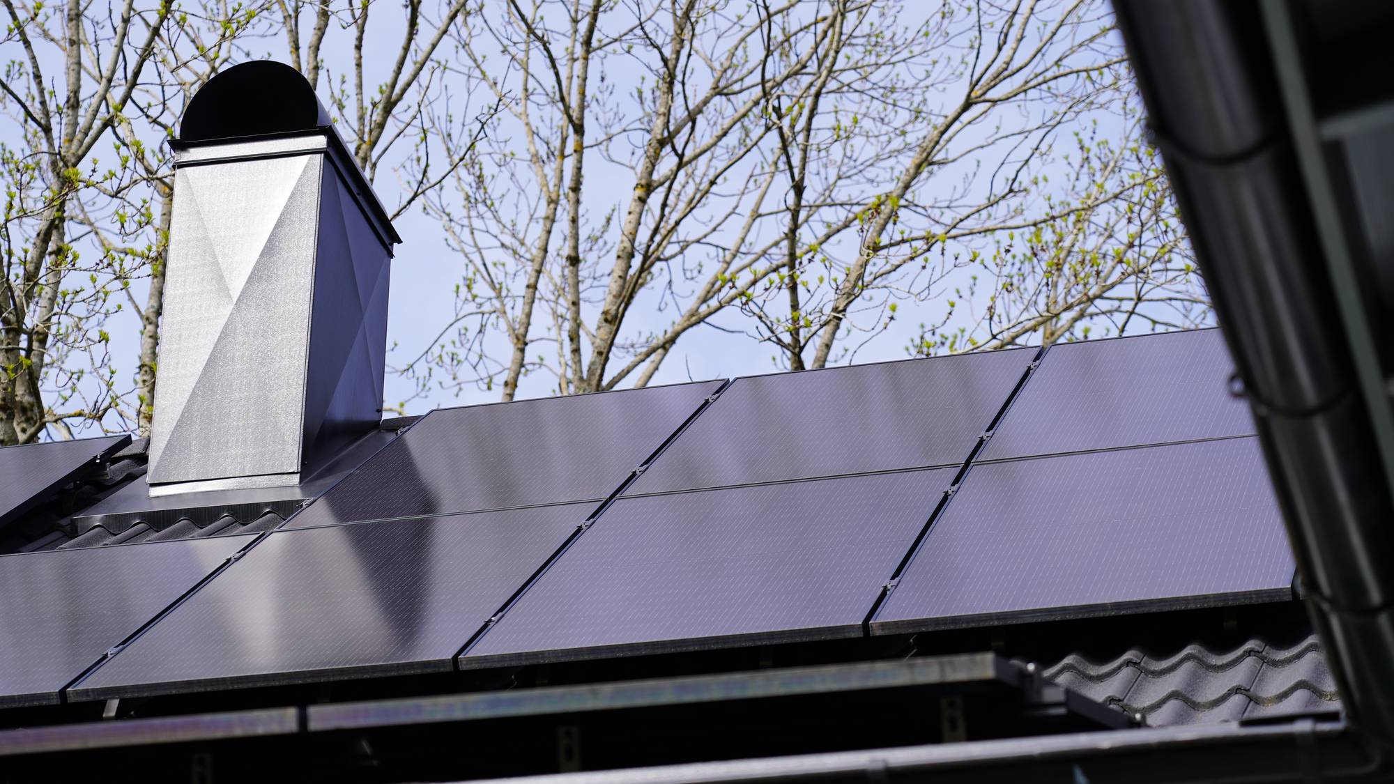 Tak med solcellepanel, en pipe til venstre på taket. Trær i bakgrunnen.