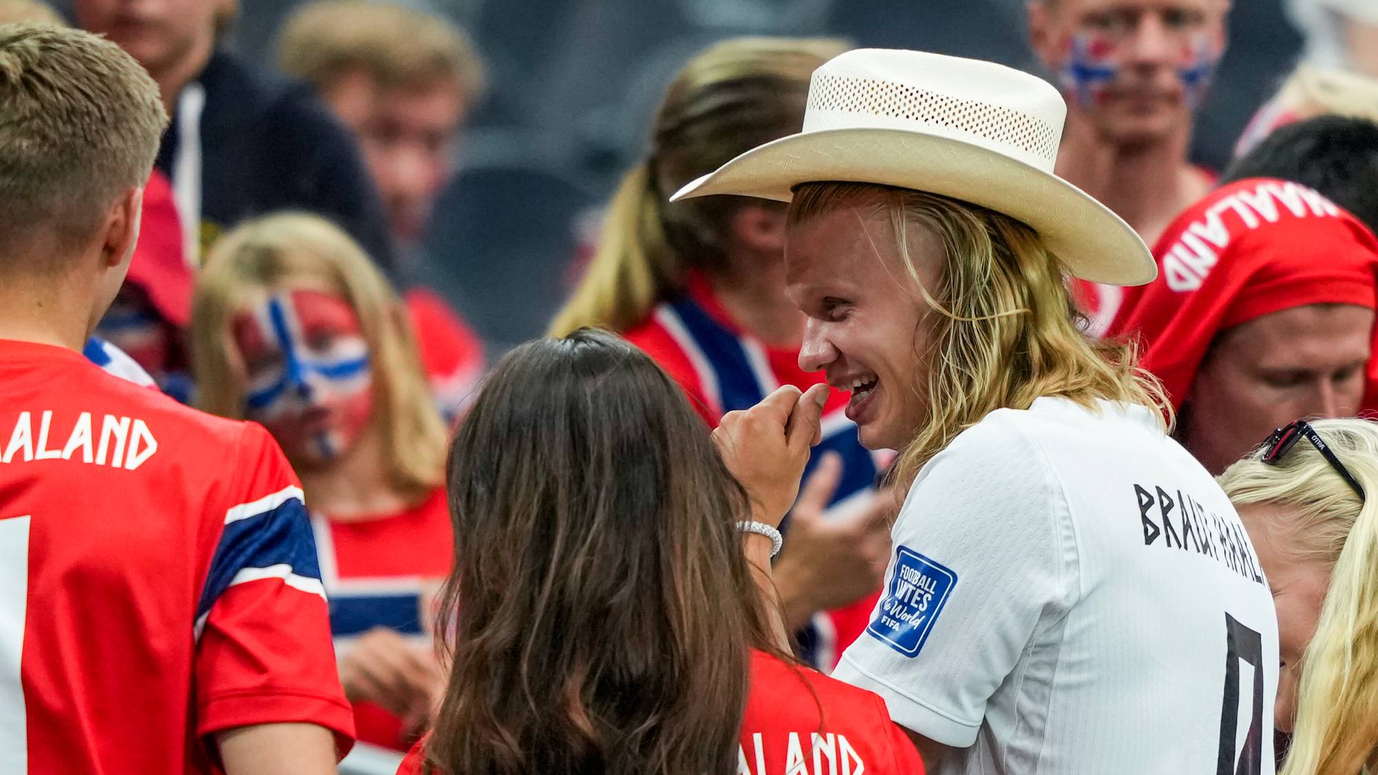 Erling Braut Haaland med cowboyhatt omgitt av supportere med norske flagg og drakter på en tribune. (Bildebeskrivelsen er laget av en KI-tjeneste)