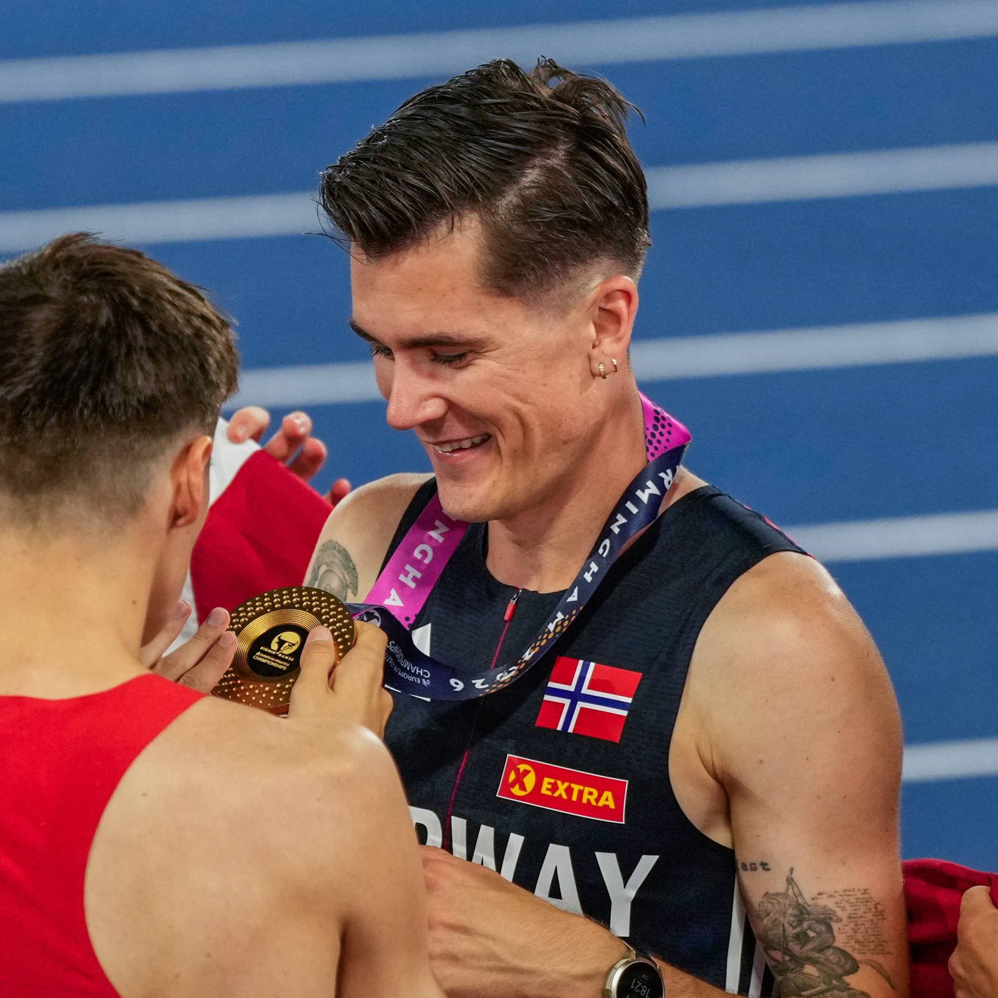 En mann med medalje rundt halsen og flere menn rundt seg på en friidrettsbane.