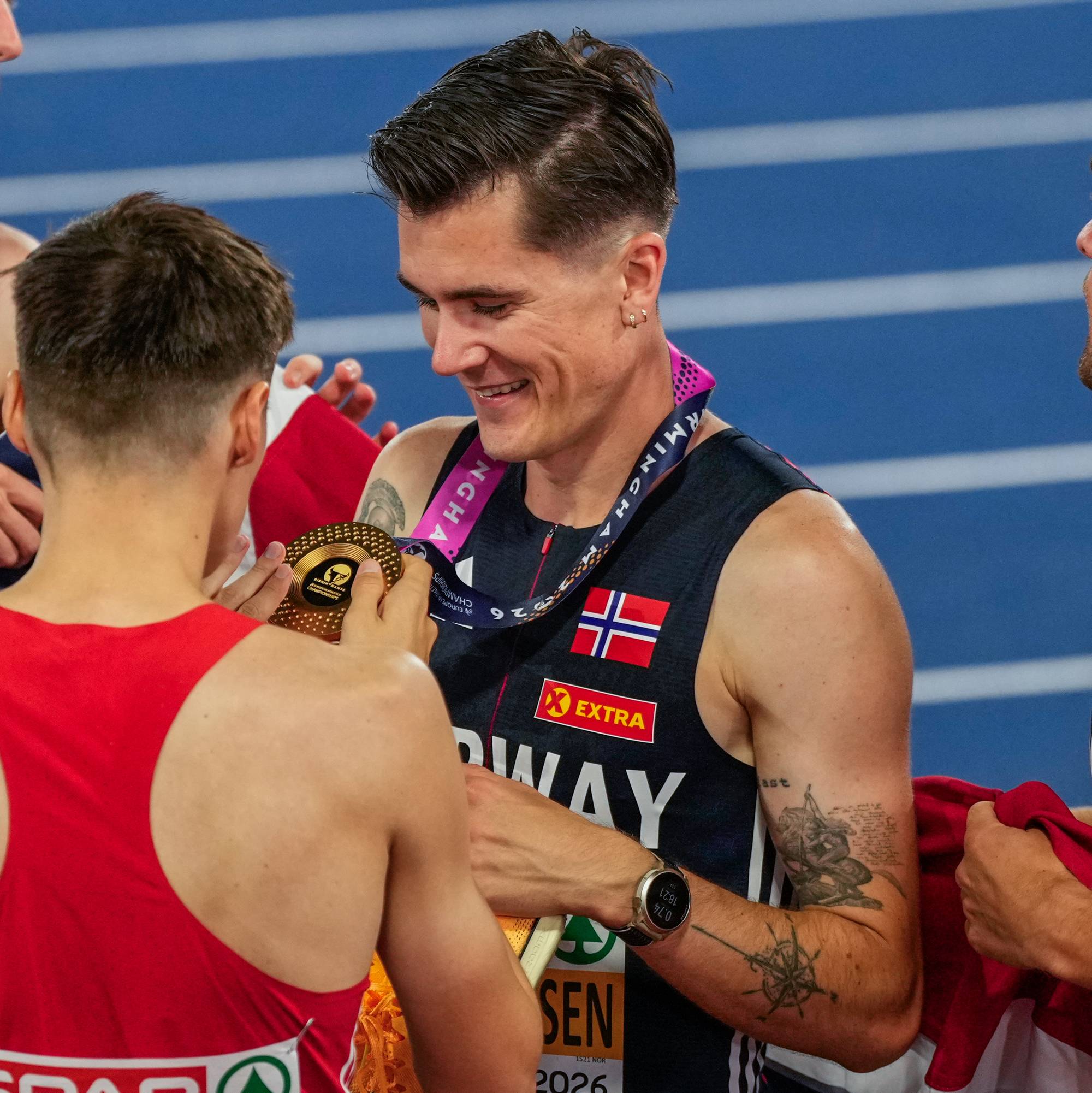 En mann med medalje rundt halsen og flere menn rundt seg på en friidrettsbane.
