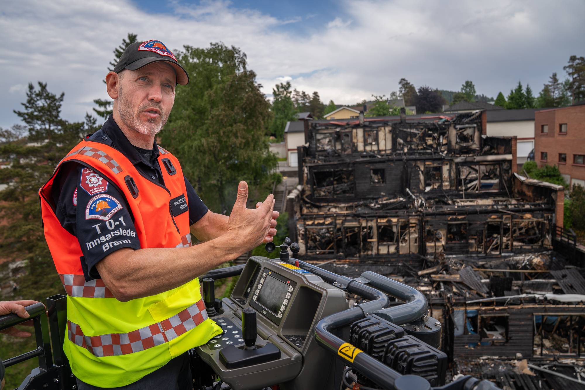 Innsatsleder Kenneth Wangen fra Nedre Romerike brann- og redningsvesen står i kurven på en lift med en utbrent terrasseblokk på Kurlandsåsen i bakgrunnen. 
