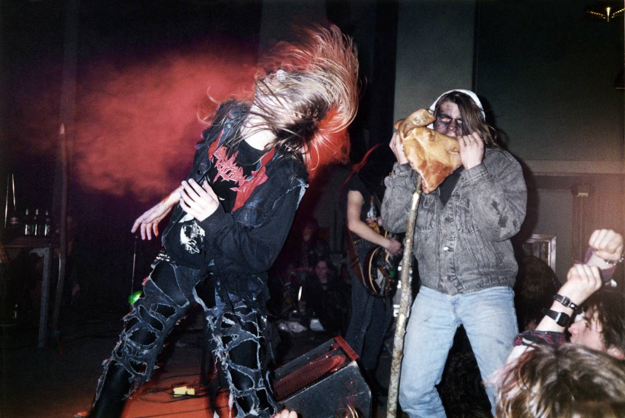 Pelle Ohlin og en ukjent publikummer på scenen under en konsert. Pelle ser ut til å være midt i en headbang, mens publikummeren later som han tar en bit av et speket grisehode bandet har tatt med seg på scenen.