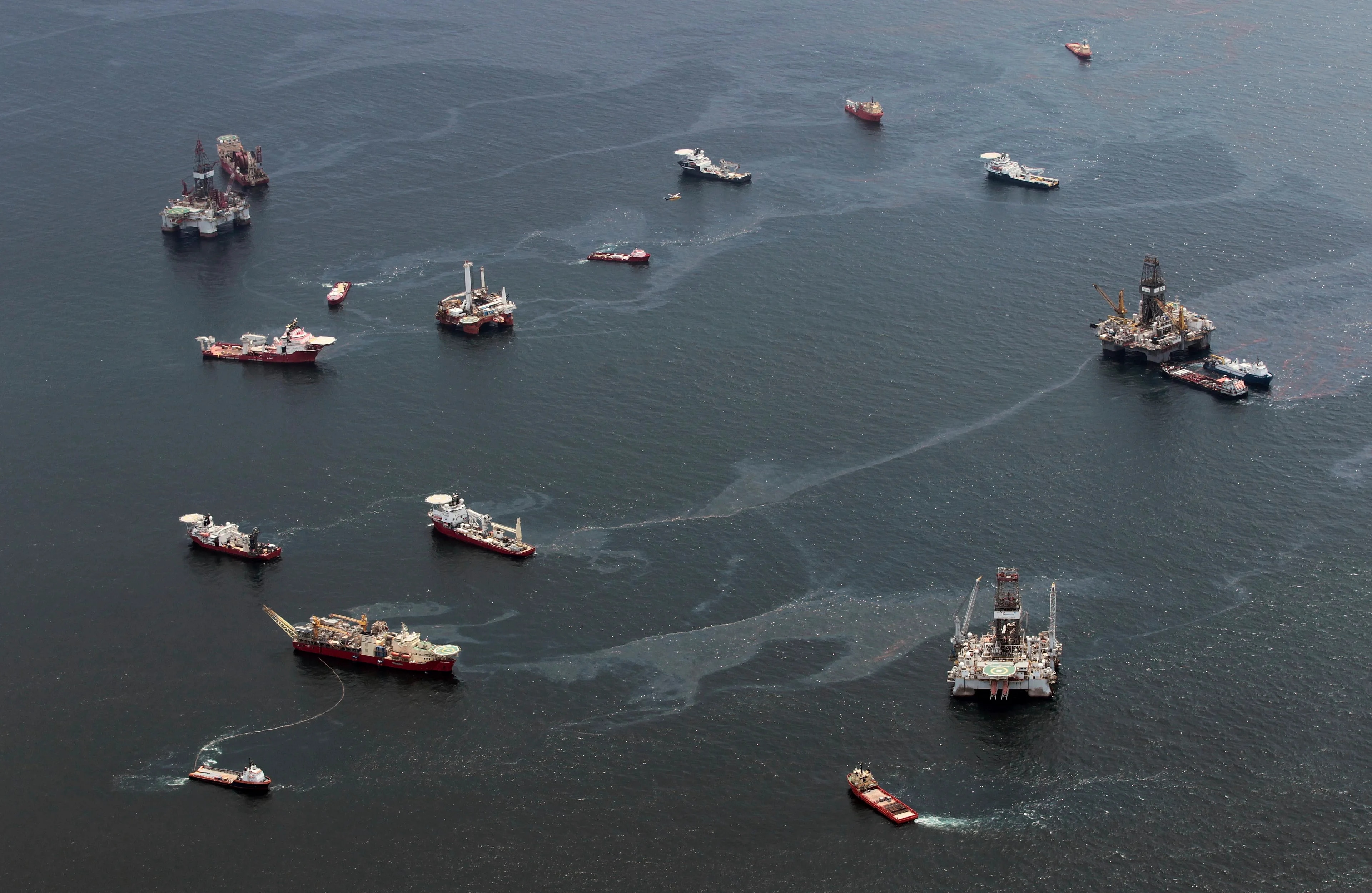 Bilder viser borerigger og offshore-båter som er omgitt av hav med store oljeflak.