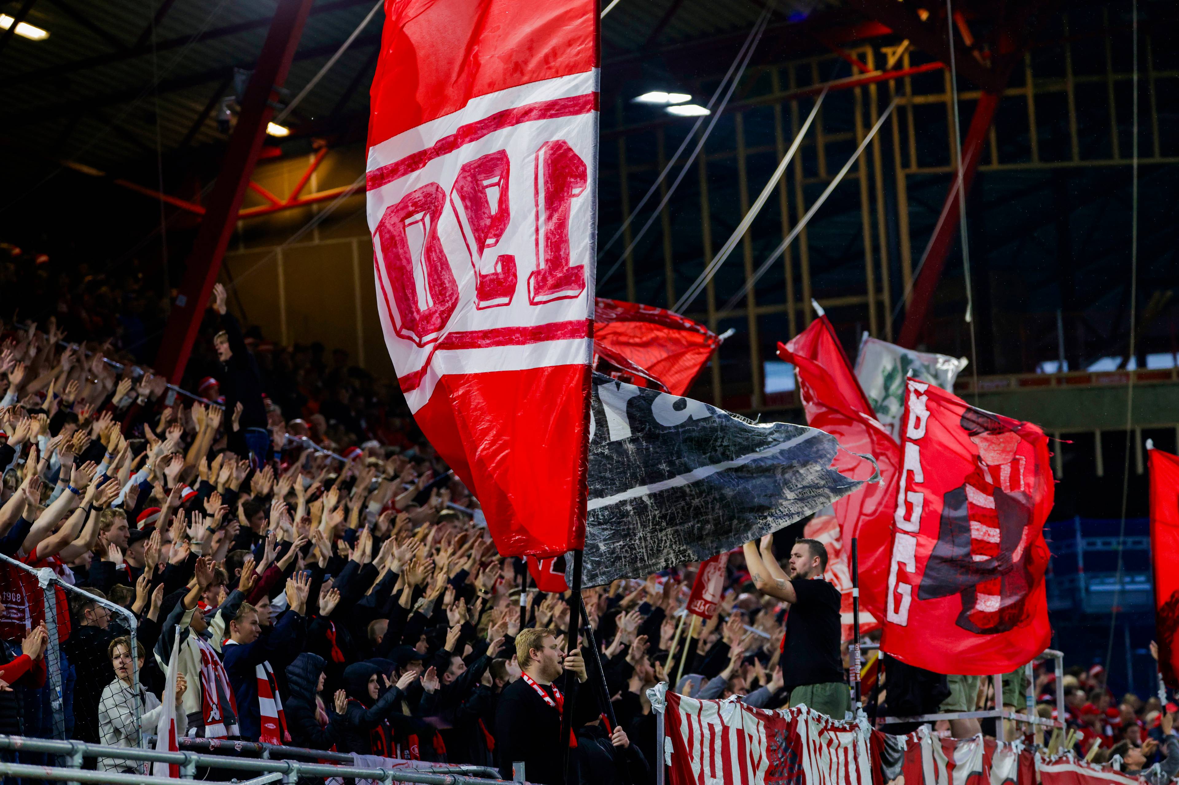 Fotballsupportere i røde klær heier med flagg på en tribune. (Bildebeskrivelsen er laget av en KI-tjeneste)