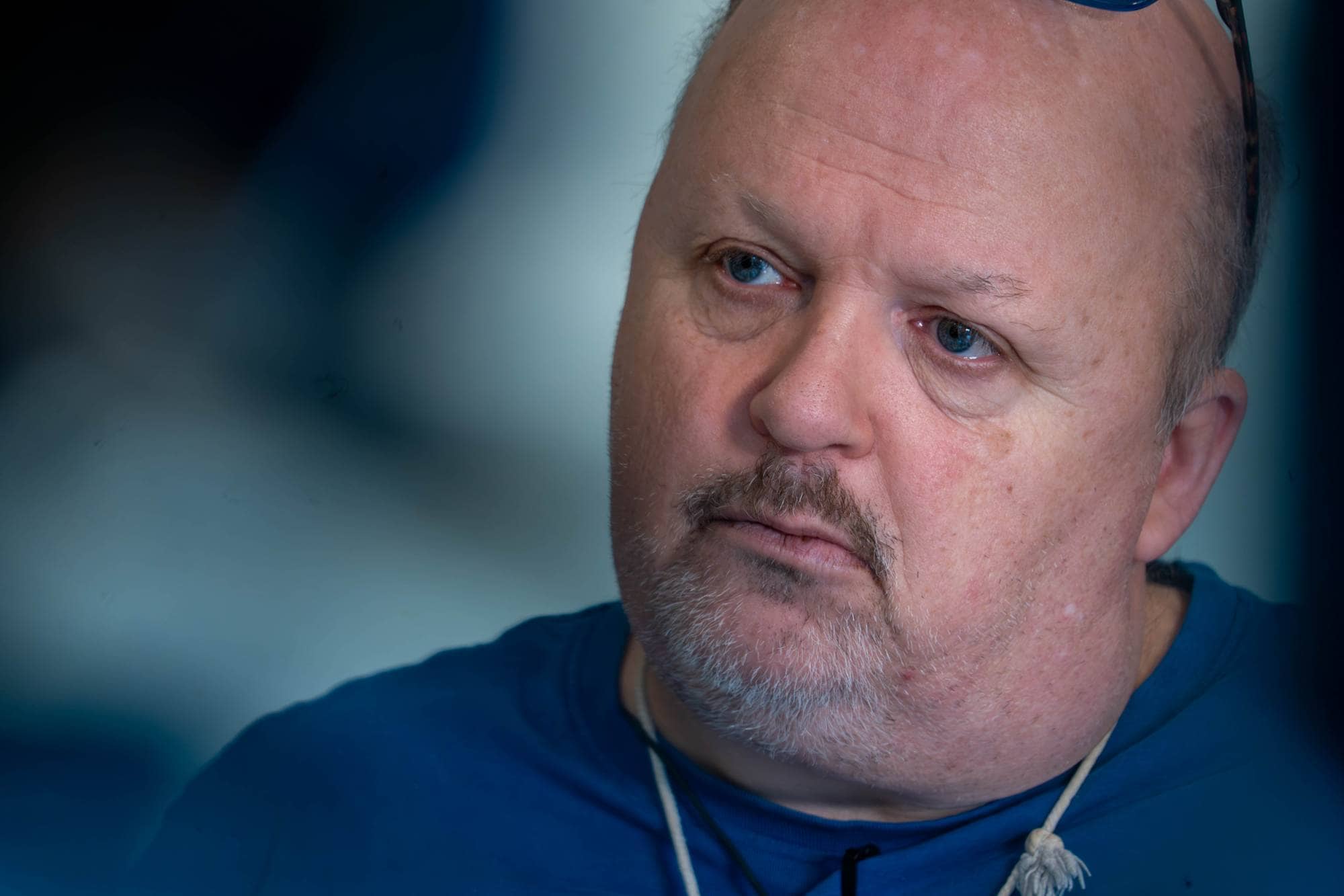 En mann med blå øyne og skjegg.
Han har på seg en blå genser.
Bakgrunnen er utydelig og mørkeblå.
Bildet er et nærbilde av ansiktet hans.