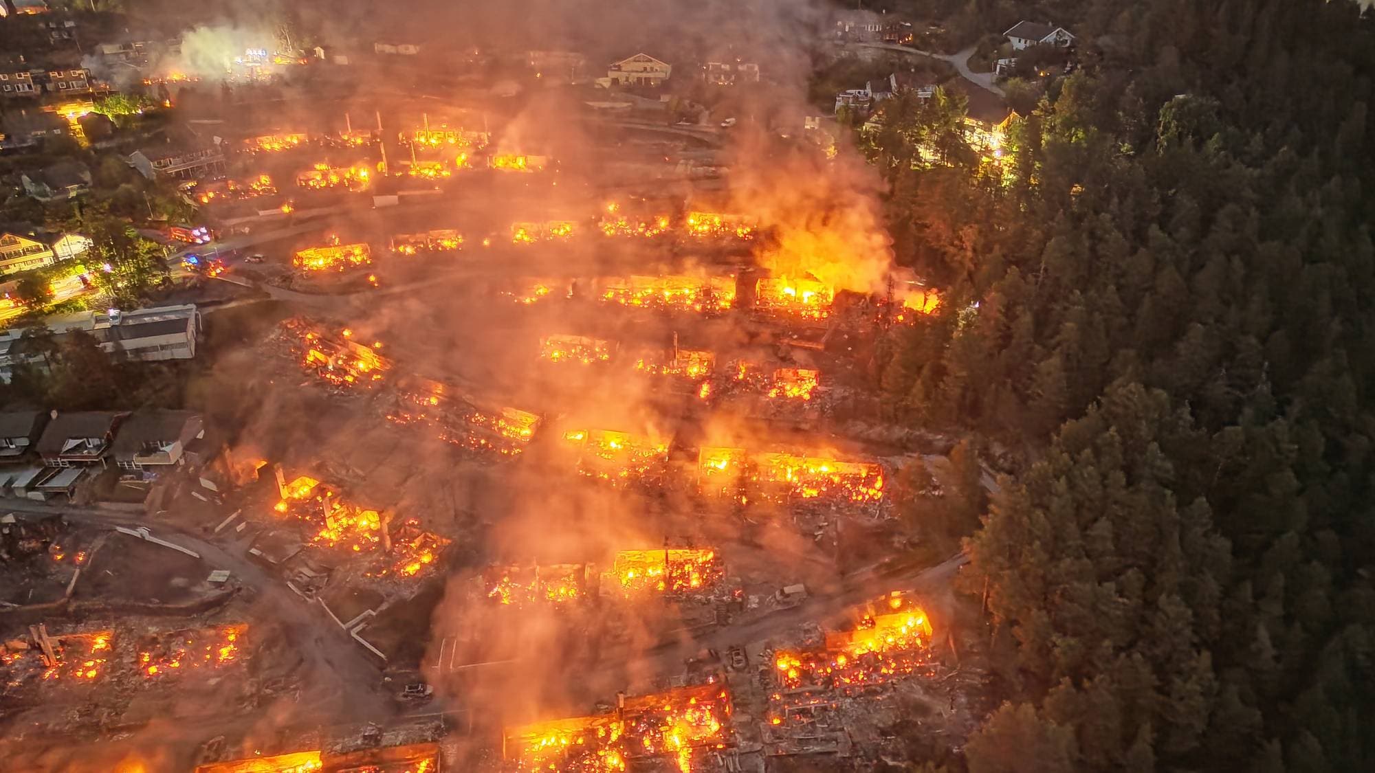Luftfoto av en stor brann i et boligområde om natten med flammer og røyk over flere bygninger. 