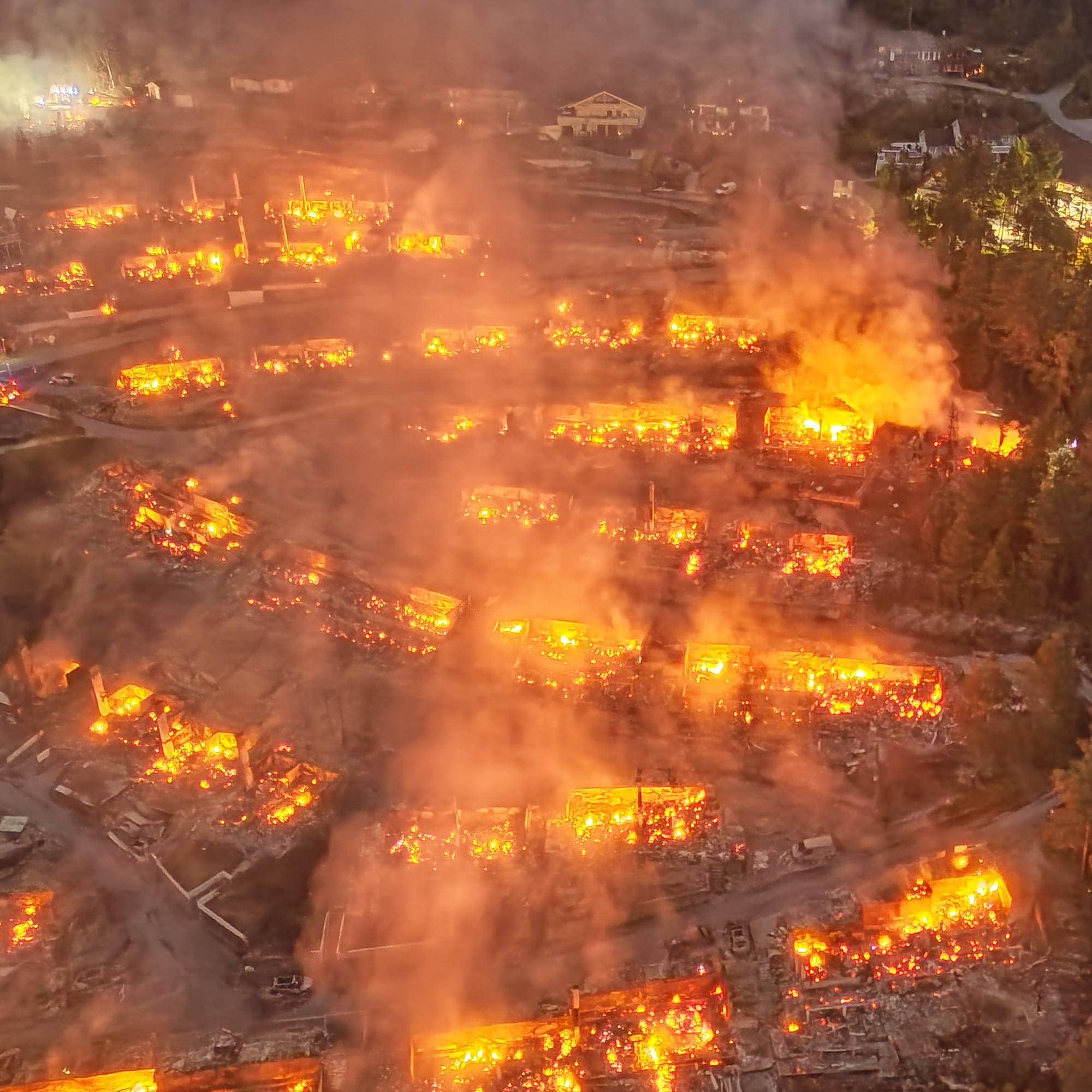 Luftfoto av en stor brann i et boligområde om natten med flammer og røyk over flere bygninger. 
