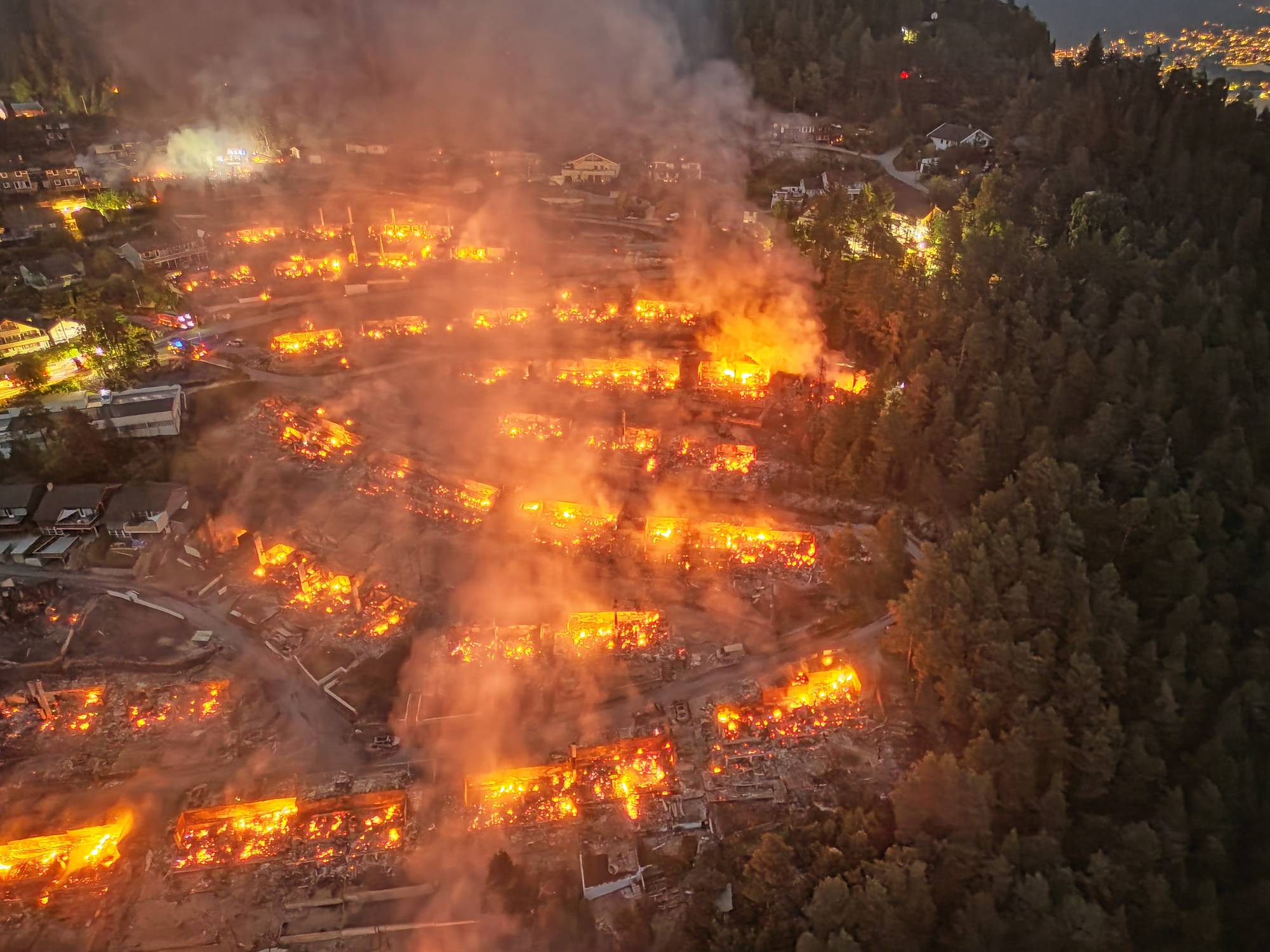 Luftfoto av en stor brann i et boligområde om natten med flammer og røyk over flere bygninger. 