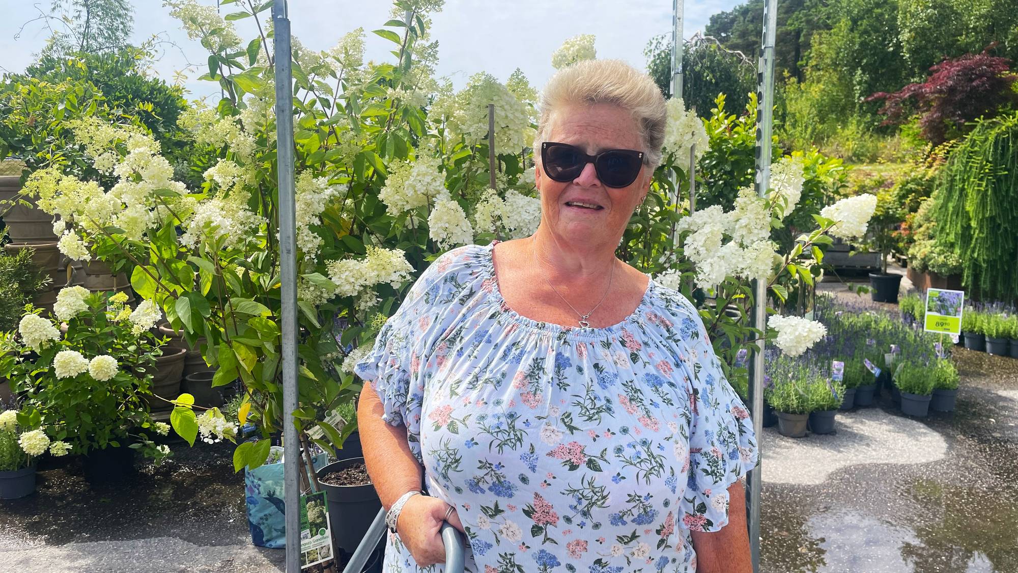 En dame med solbriller står foran blomster