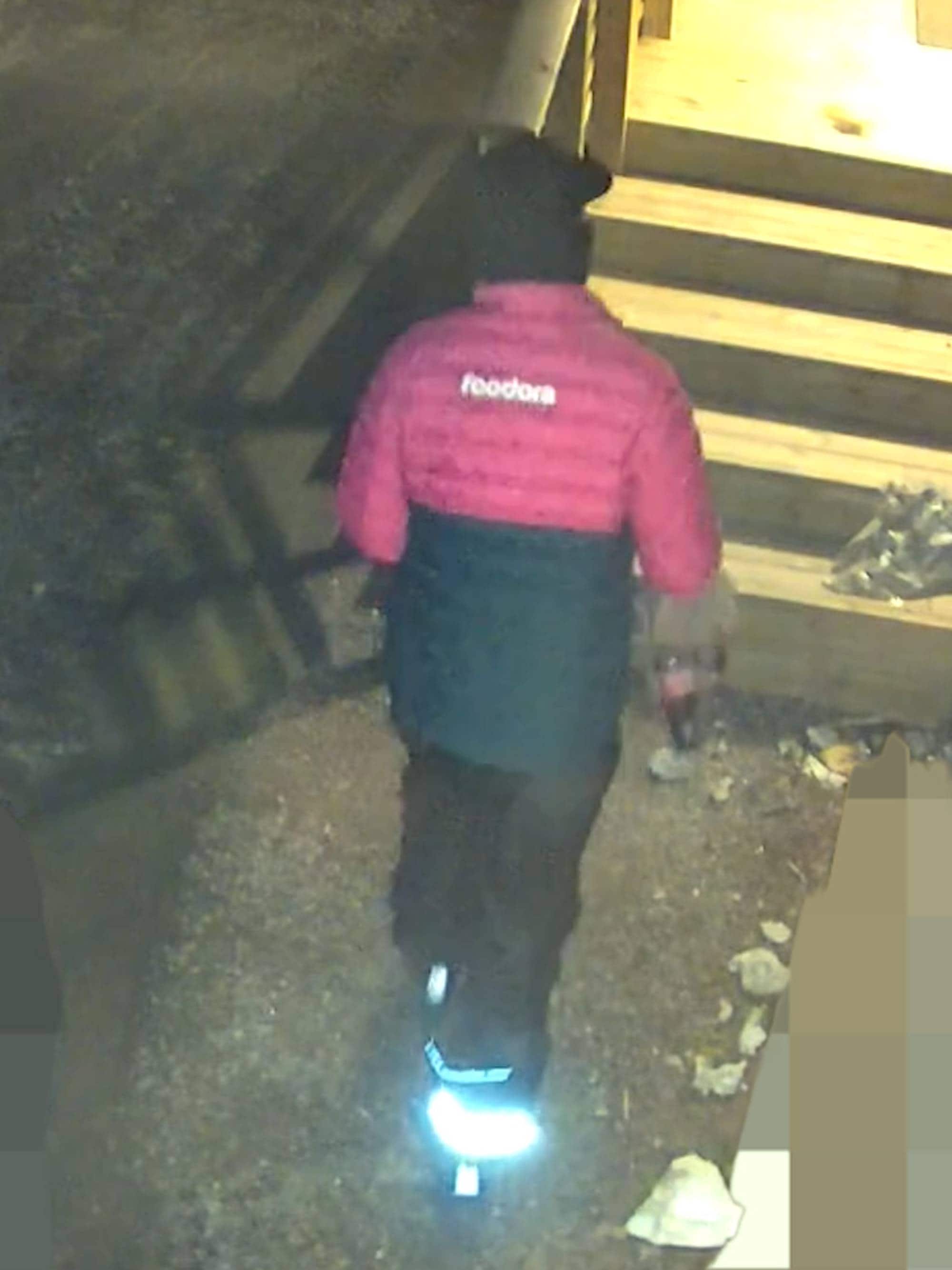 På bildet ser man en man med rosa Foodora-jakke, mørk caps og mørk bukse. I hånden har han en pose med cola.
