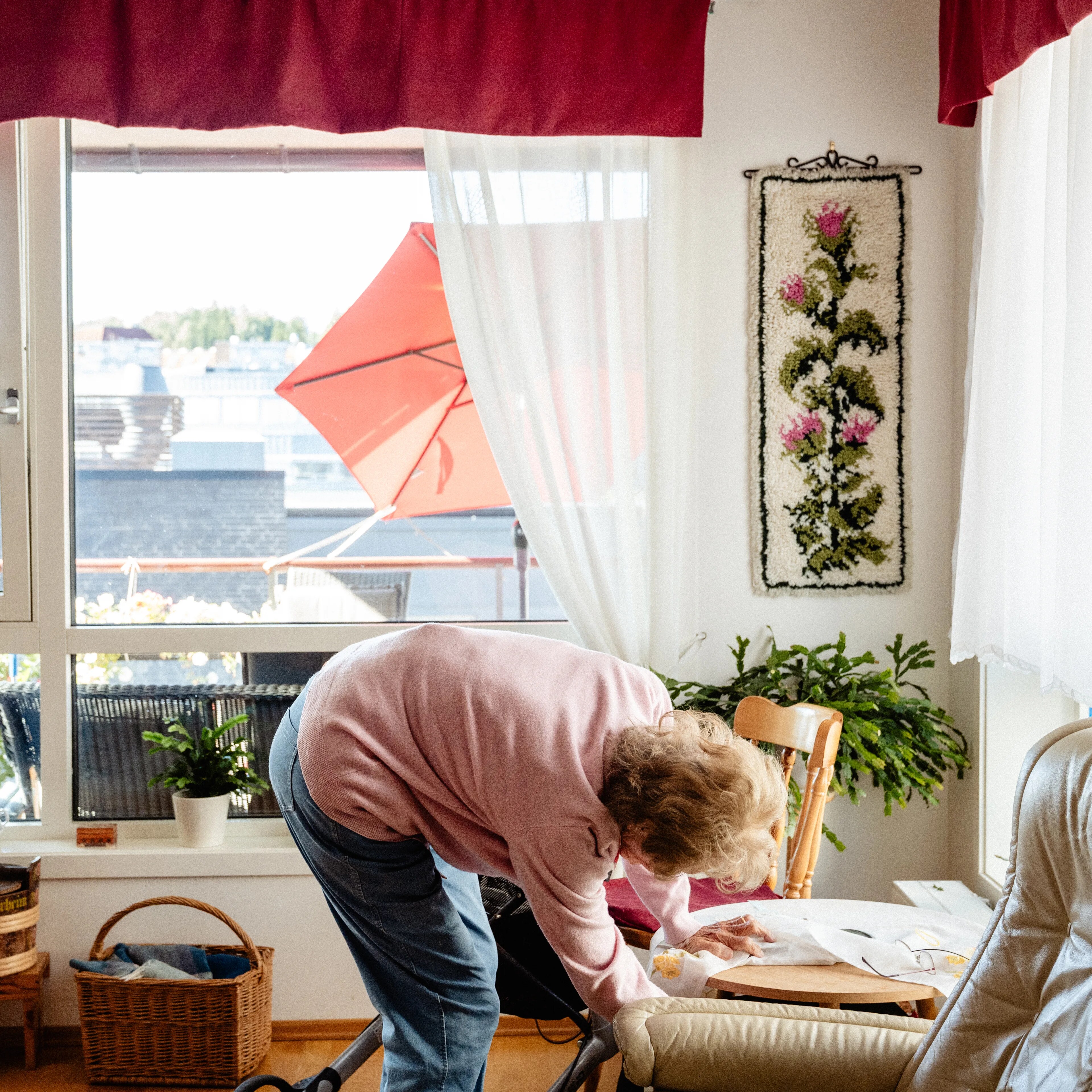 Eldre kvinne lener seg over et bord i en stue med utsikt mot en balkong. (Bildebeskrivelsen er laget av en KI-tjeneste)