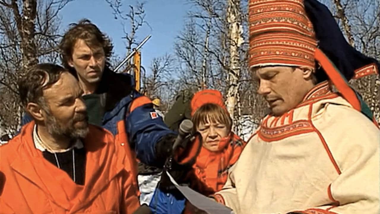 Ole Henrik Magga snakker til mann kledd i rød anorakk. Reporter og kvinne i bakgrunnen.